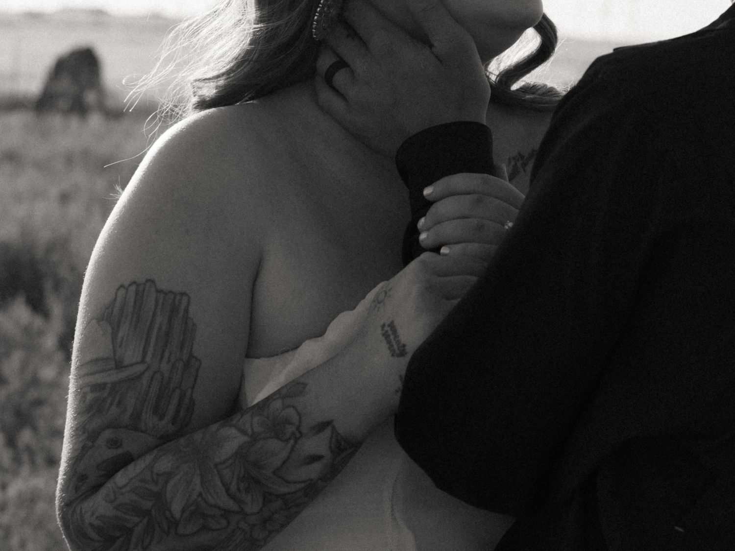 Black and white photo of a couple embracing closely, the woman showing elaborate tattoos on her arm.