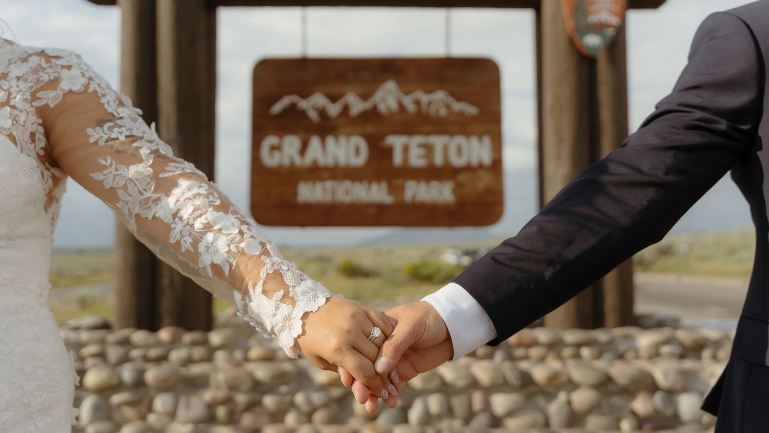 Bride and groom holding hands in front of the Grand Teton National Park entrance sign.