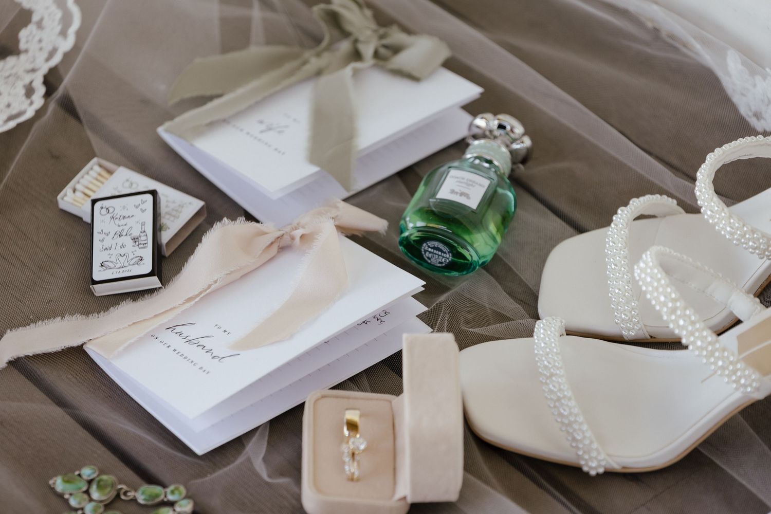 Flat lay of wedding accessories including shoes, perfume, rings, and veil.