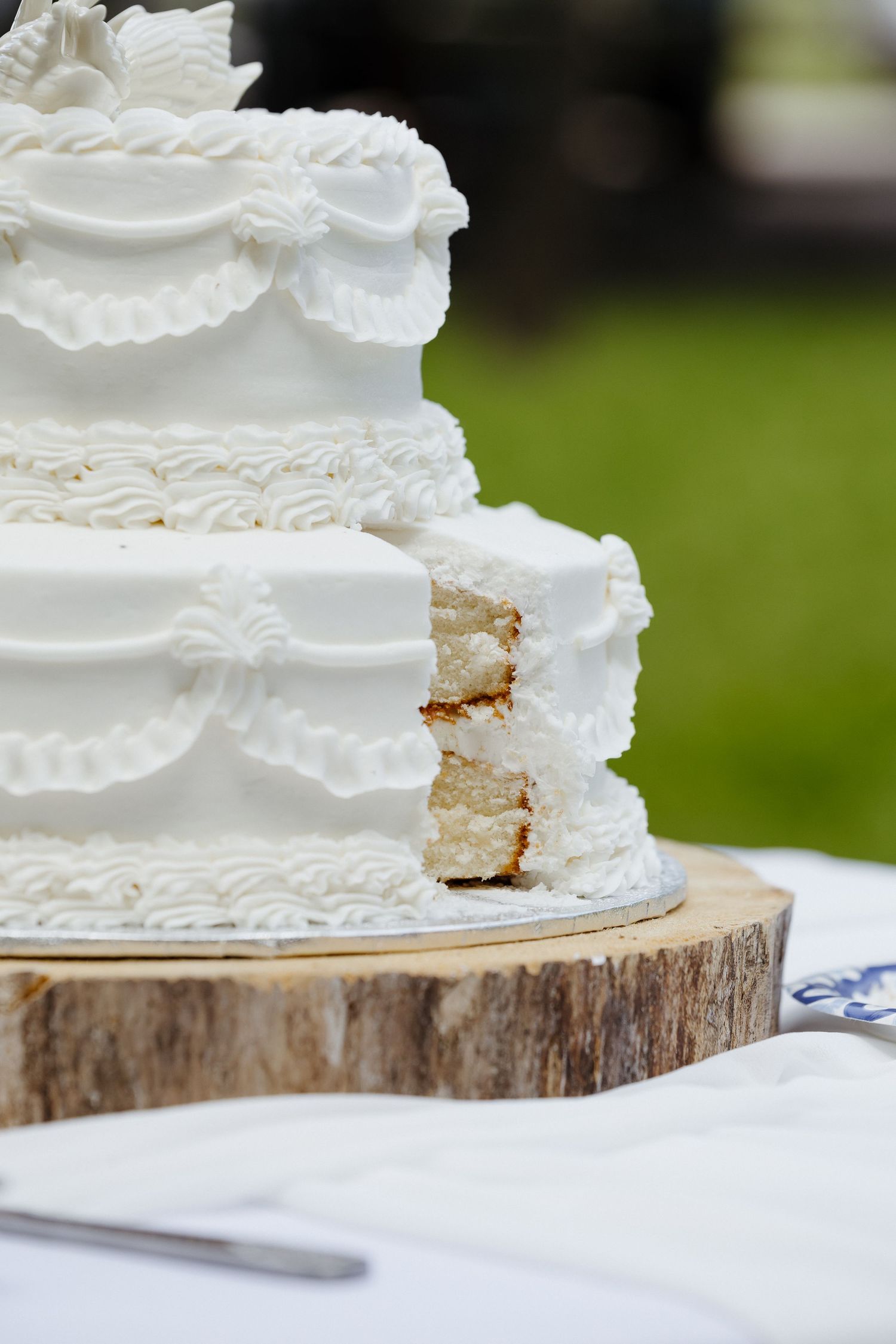 Elegant two-tier white wedding cake with swan toppers and decorative frosting, displayed on a rustic wood slice stand.