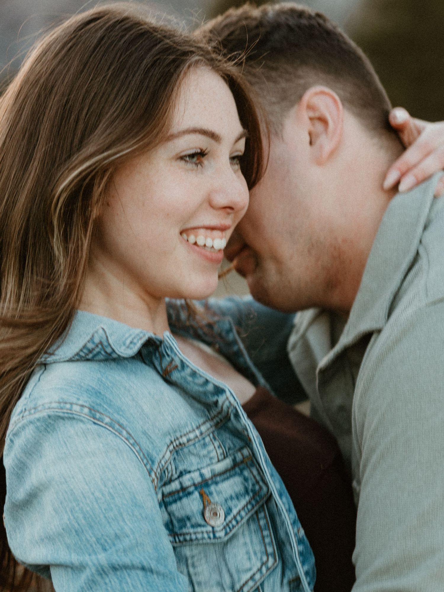 Close-up of smiling woman leaning toward her partner with soft golden bokeh light in the background.