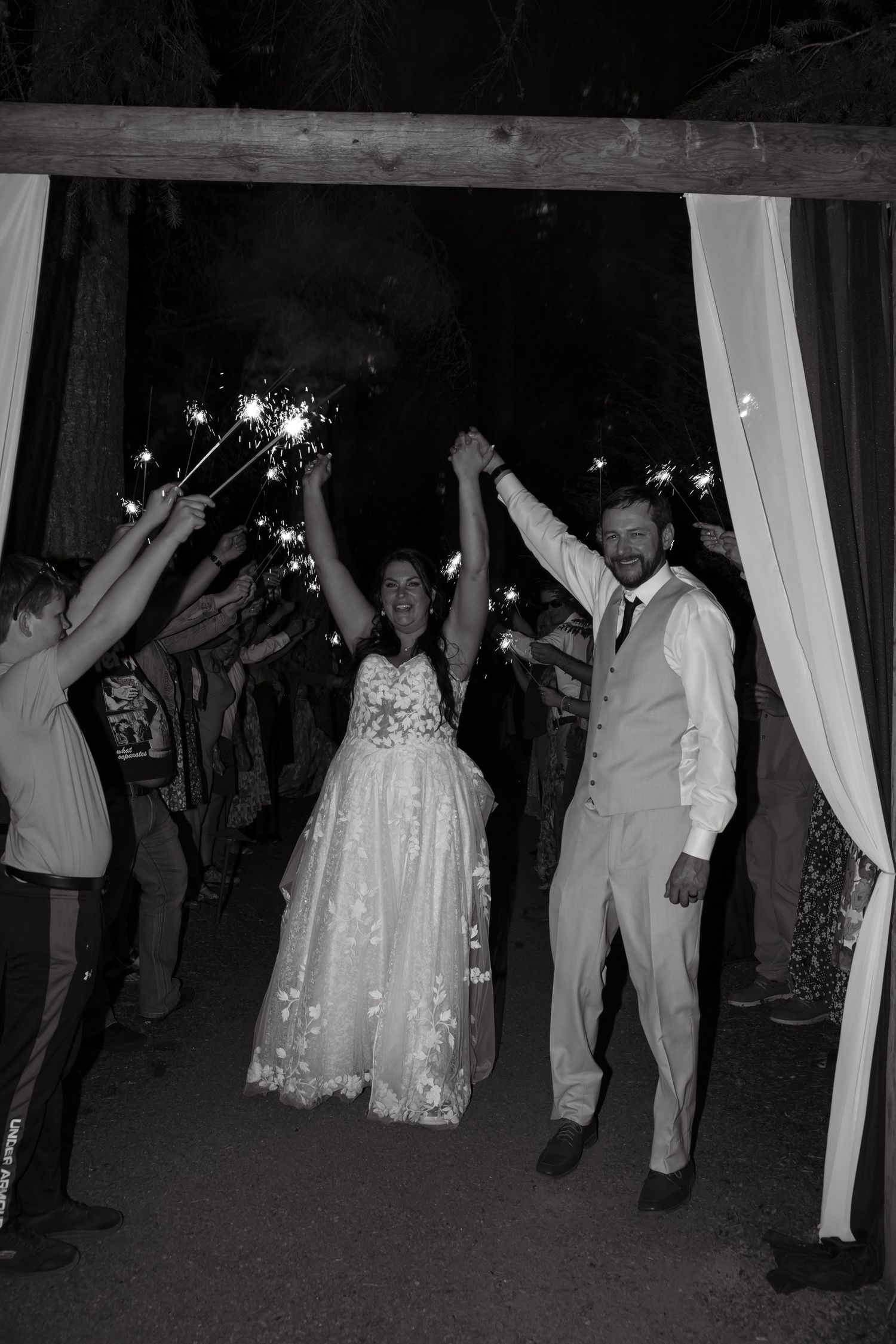 Black and white photo of newlyweds walking through sparkler send-off at night.