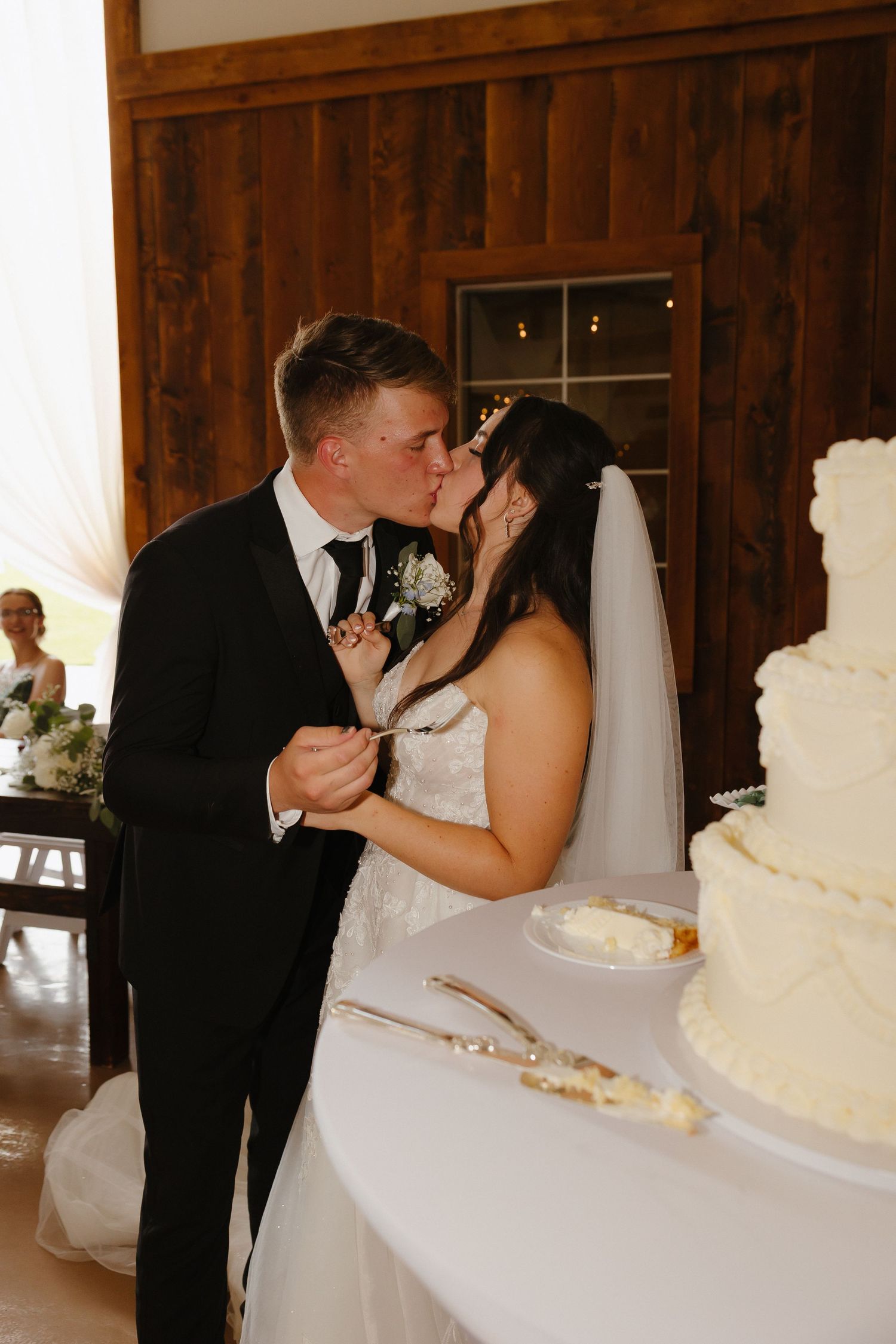 Bride and groom share a kiss while cutting their white wedding cake together.
