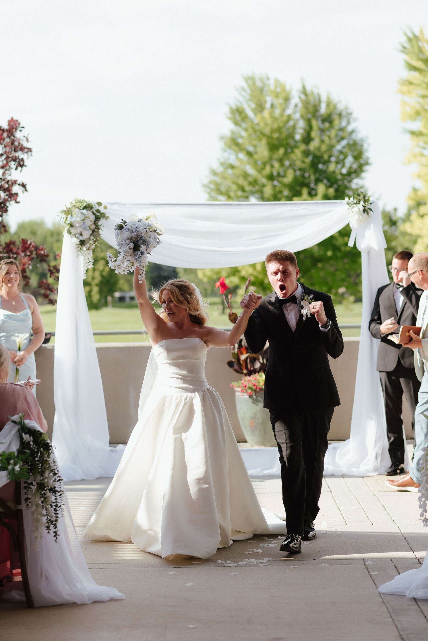Joyful bride and groom celebrating at outdoor wedding ceremony under white draped arch.
