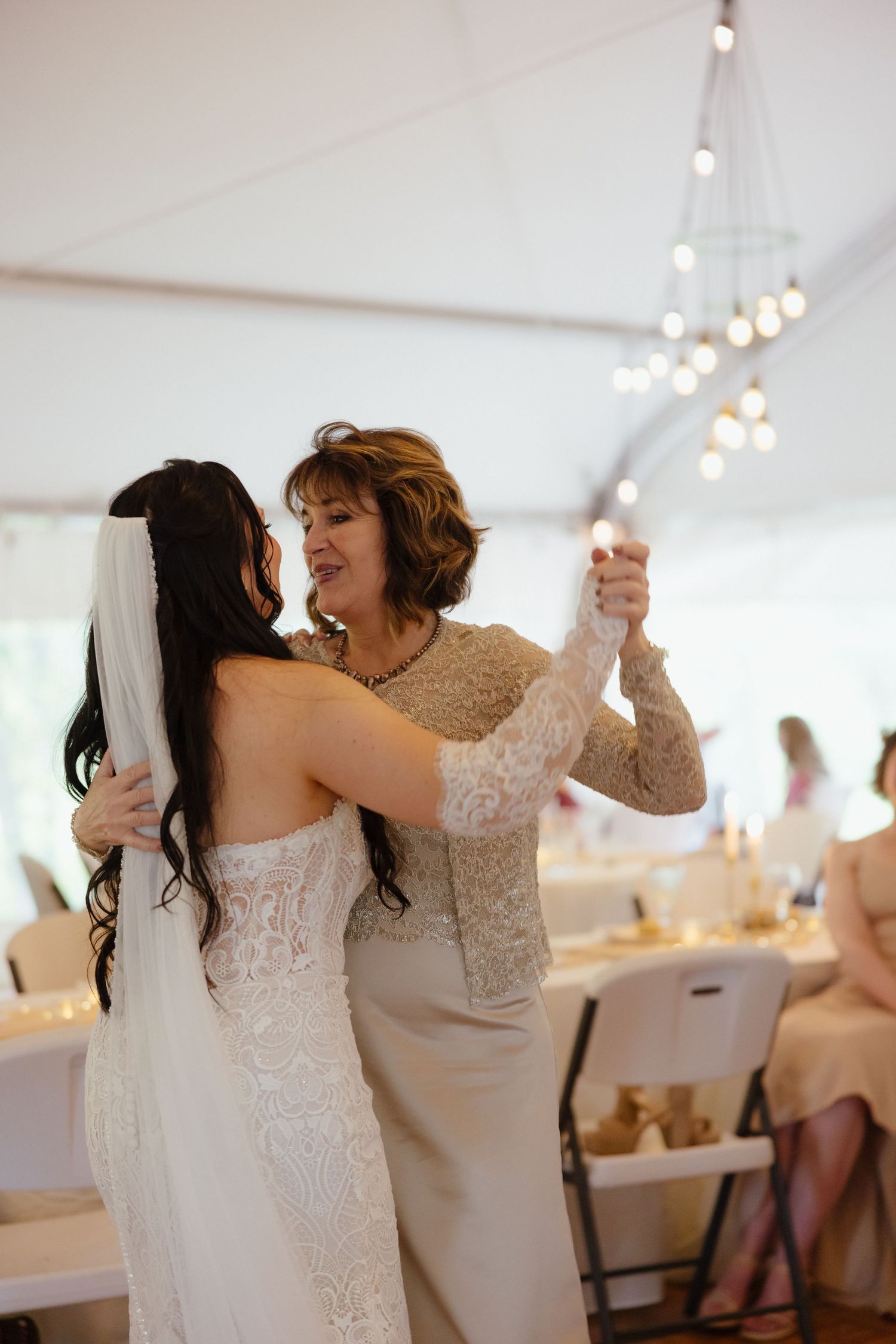 Bride and mother sharing an emotional first dance at elegant tented wedding reception with string lights.