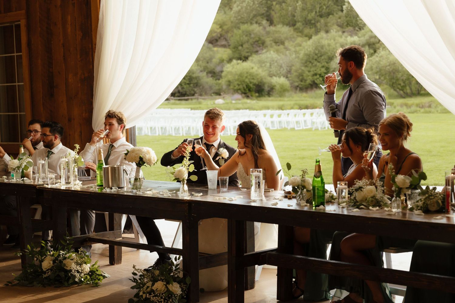 Wedding party seated at head table during reception toast with champagne and floral centerpieces.
