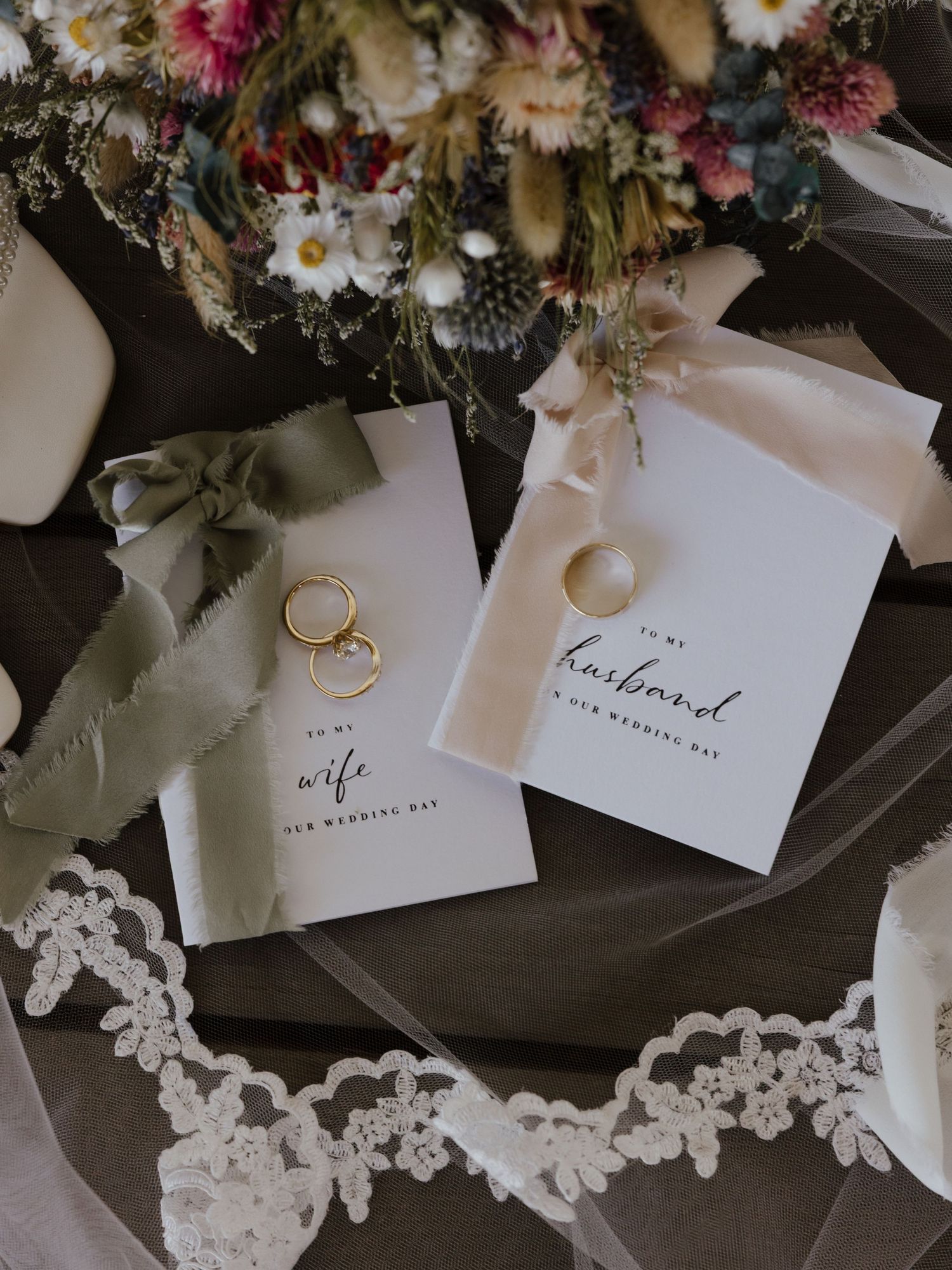 Wedding flat lay with gold rings, to my wife and husband cards, lace veil and floral bouquet.