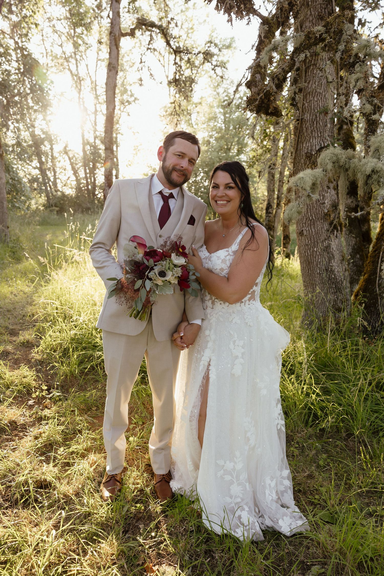 Bride and groom posing together in sun-dappled forest with moss-covered trees during golden hour wedding portraits.