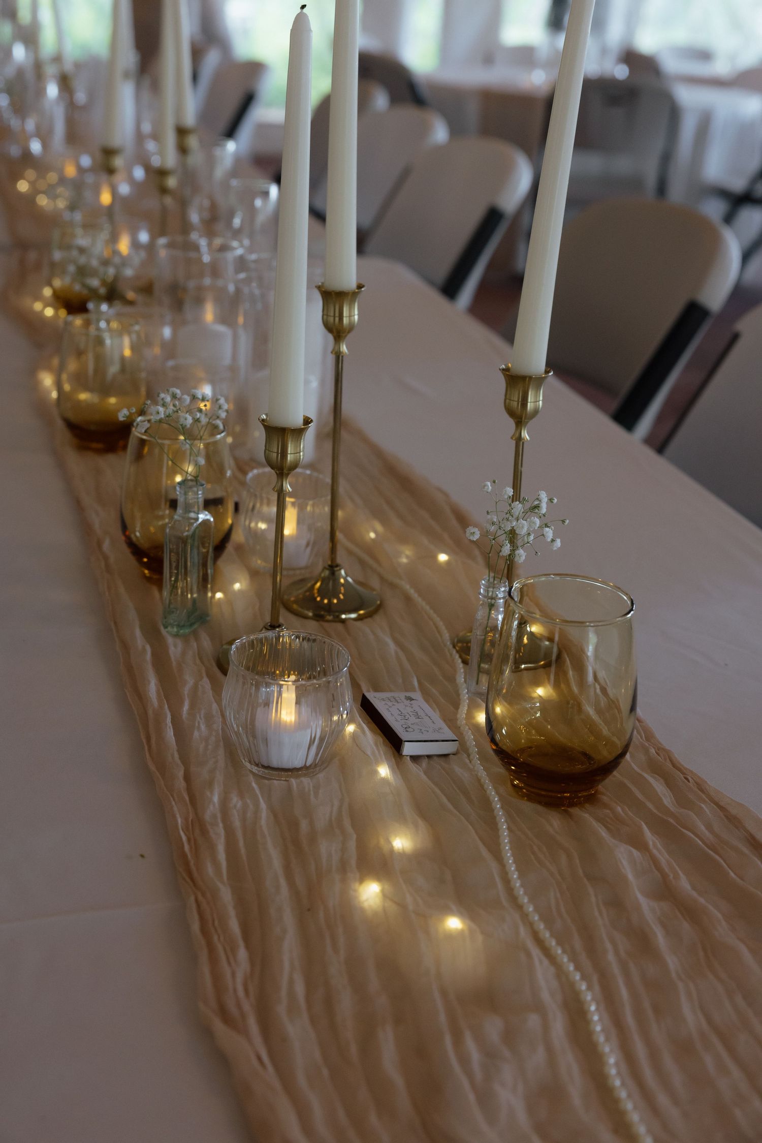 Elegant wedding reception table decorated with gold candlesticks, amber glassware, and fairy lights.