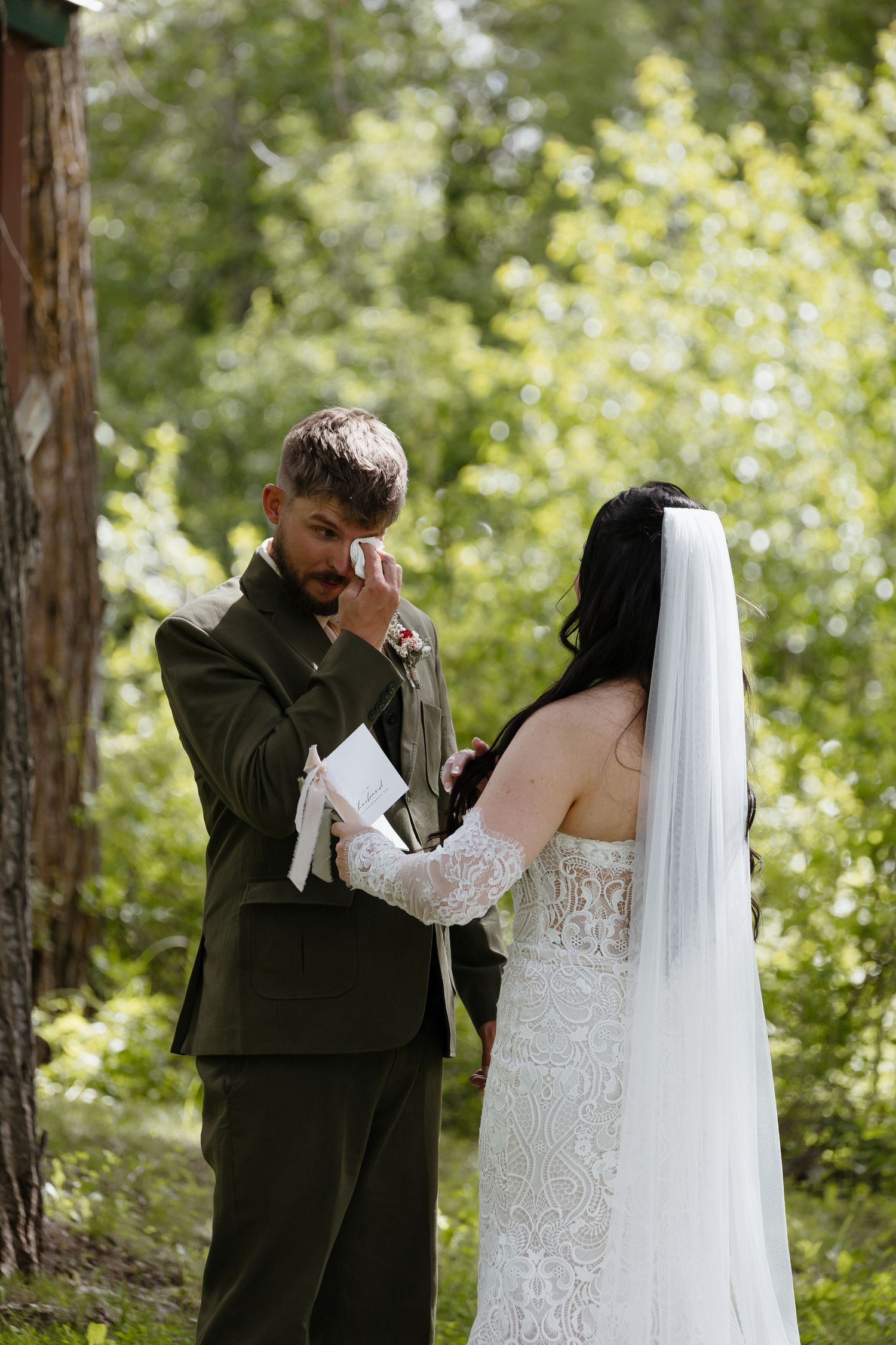 Emotional groom wiping tears while bride holds his hand during vow exchange.