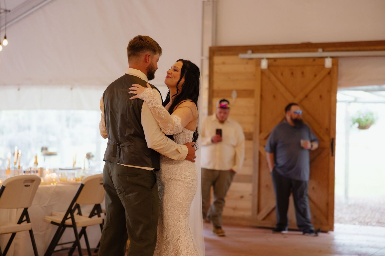 Bride and groom share first dance at rustic barn wedding venue with wooden doors.