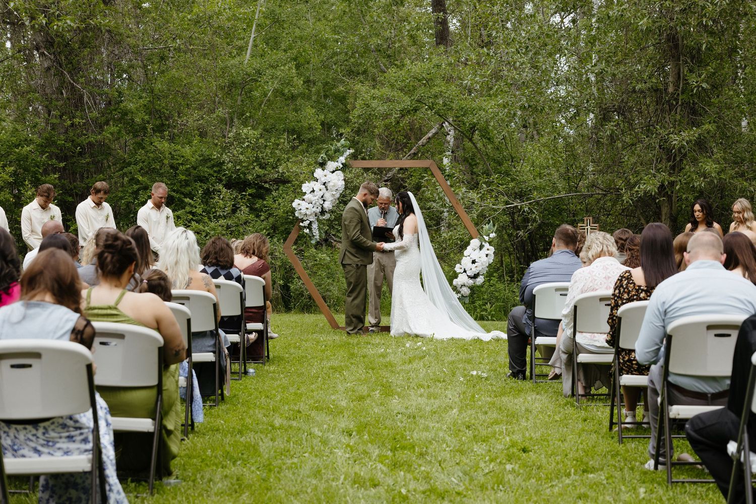 Outdoor wedding ceremony at hexagonal wooden arch with white floral decor.