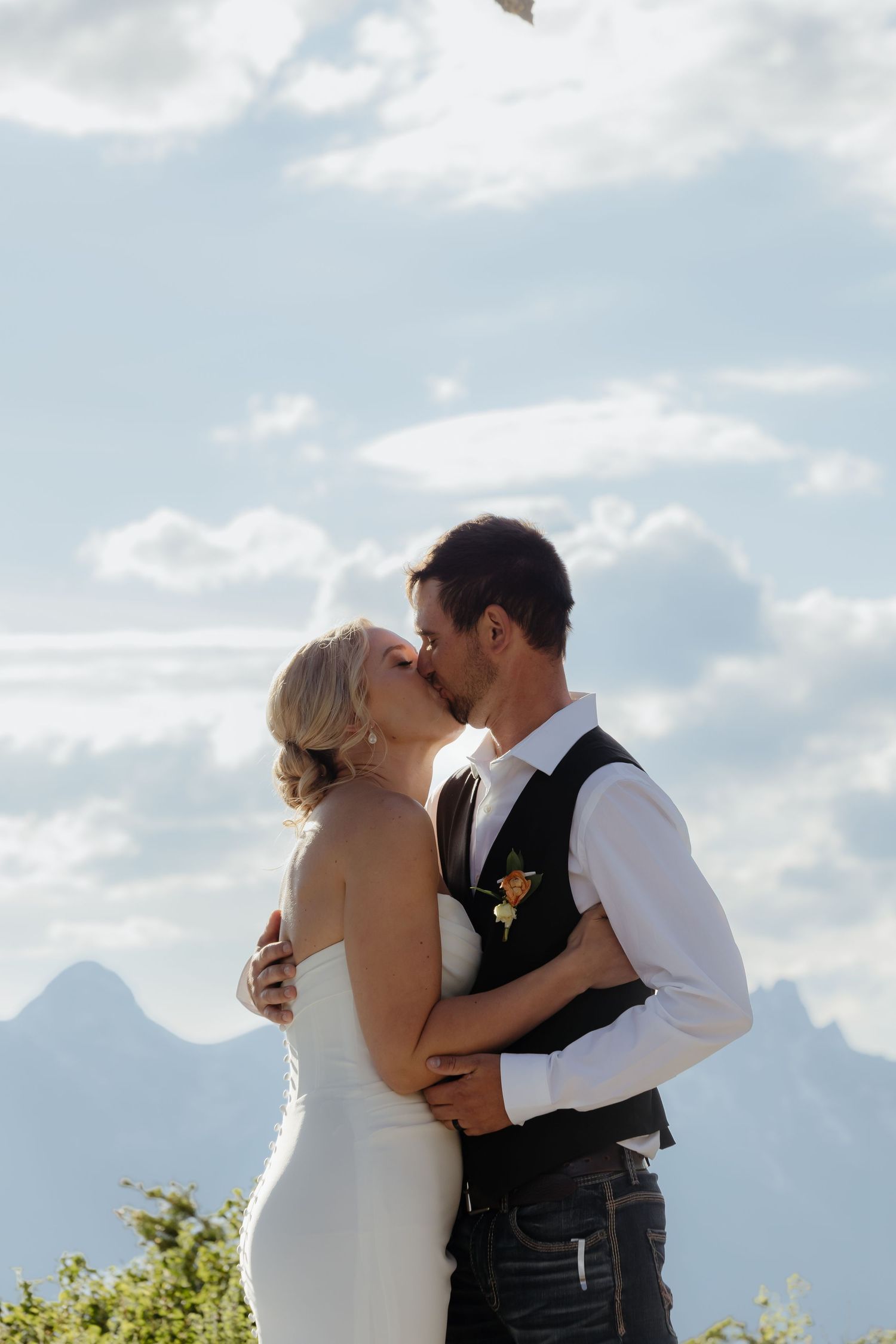 Bride and groom sharing romantic kiss with Grand Teton mountain range visible in background.