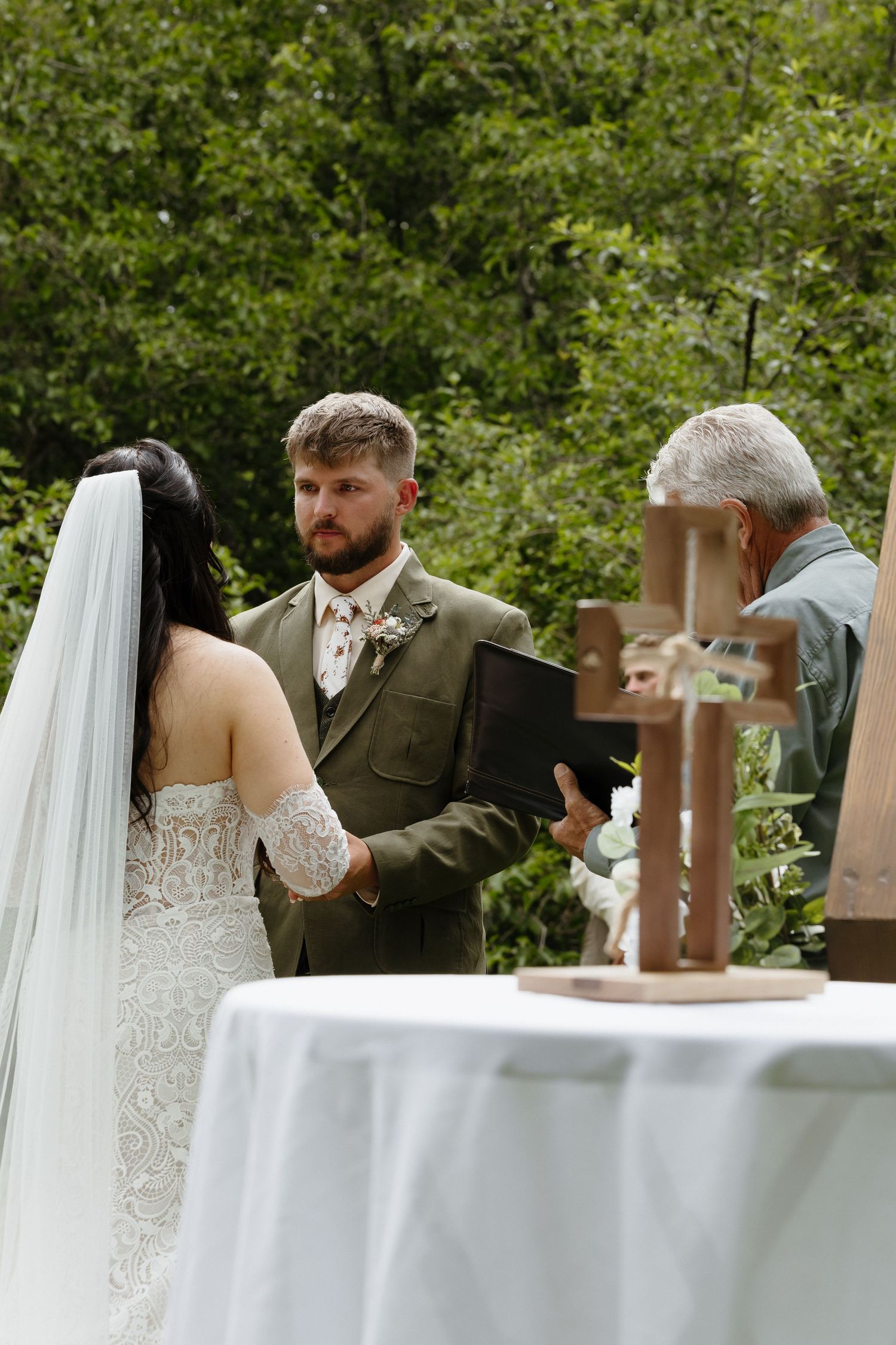 Bride and groom hold hands before officiant at outdoor wedding ceremony altar.