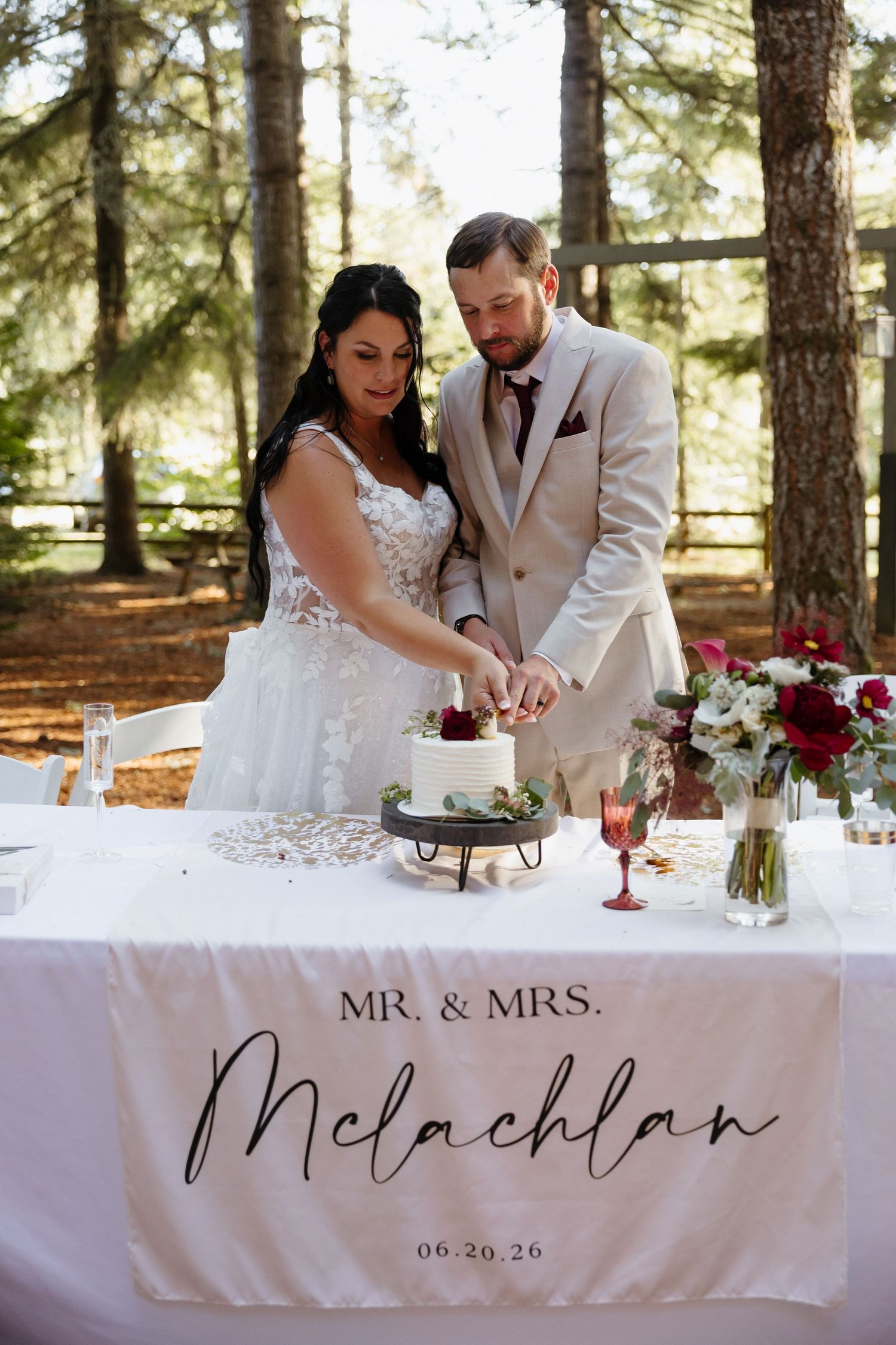Bride and groom cut white wedding cake at table with Mr. & Mrs. McLachlan banner dated 06.20.26.