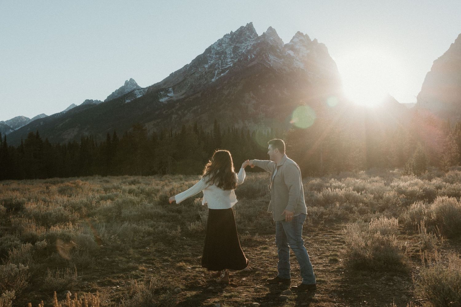 Couple twirling together in a golden meadow with dramatic mountain peaks glowing in the setting sun.