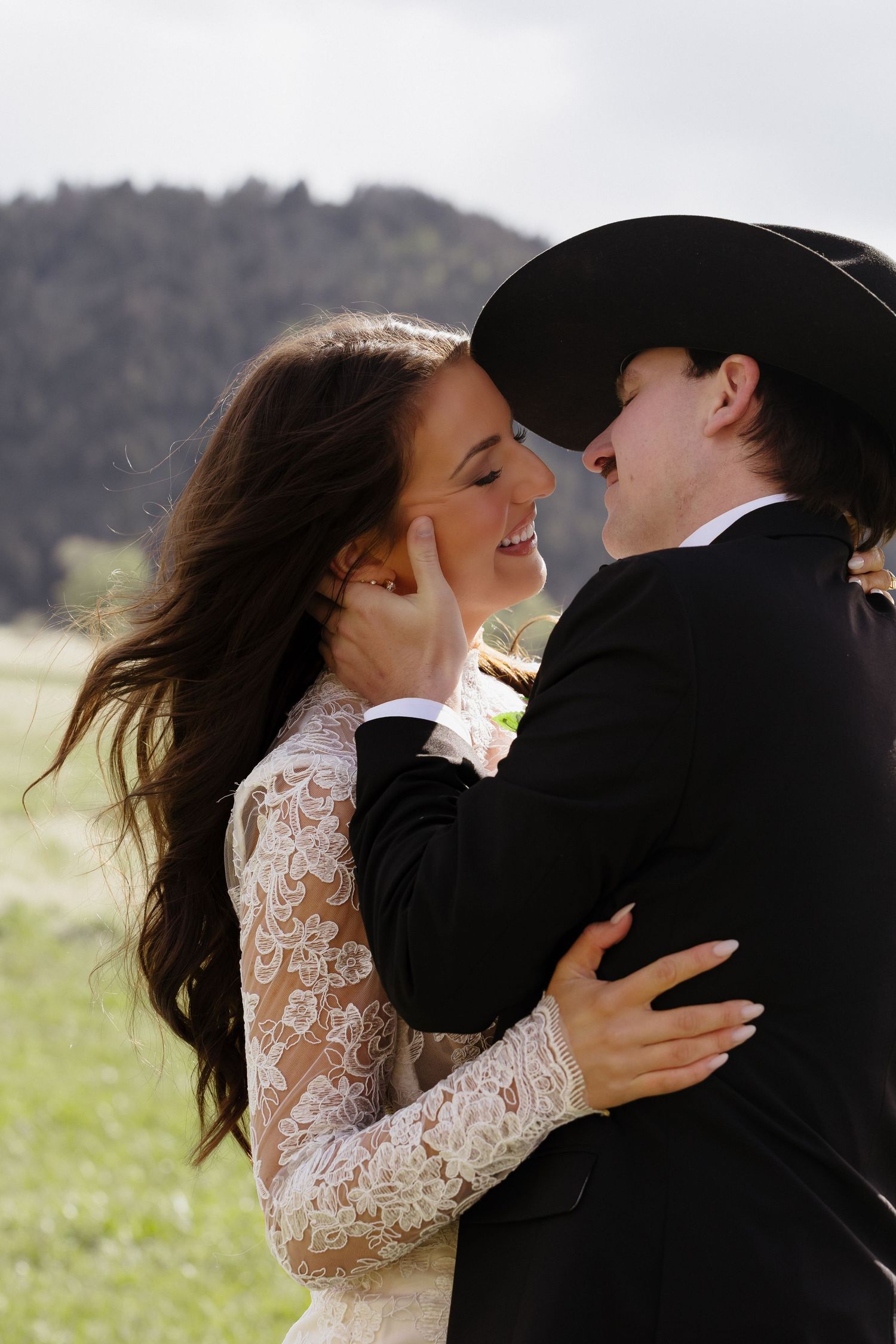 Bride and groom smile at each other tenderly as wind blows her hair at outdoor western mountain wedding.