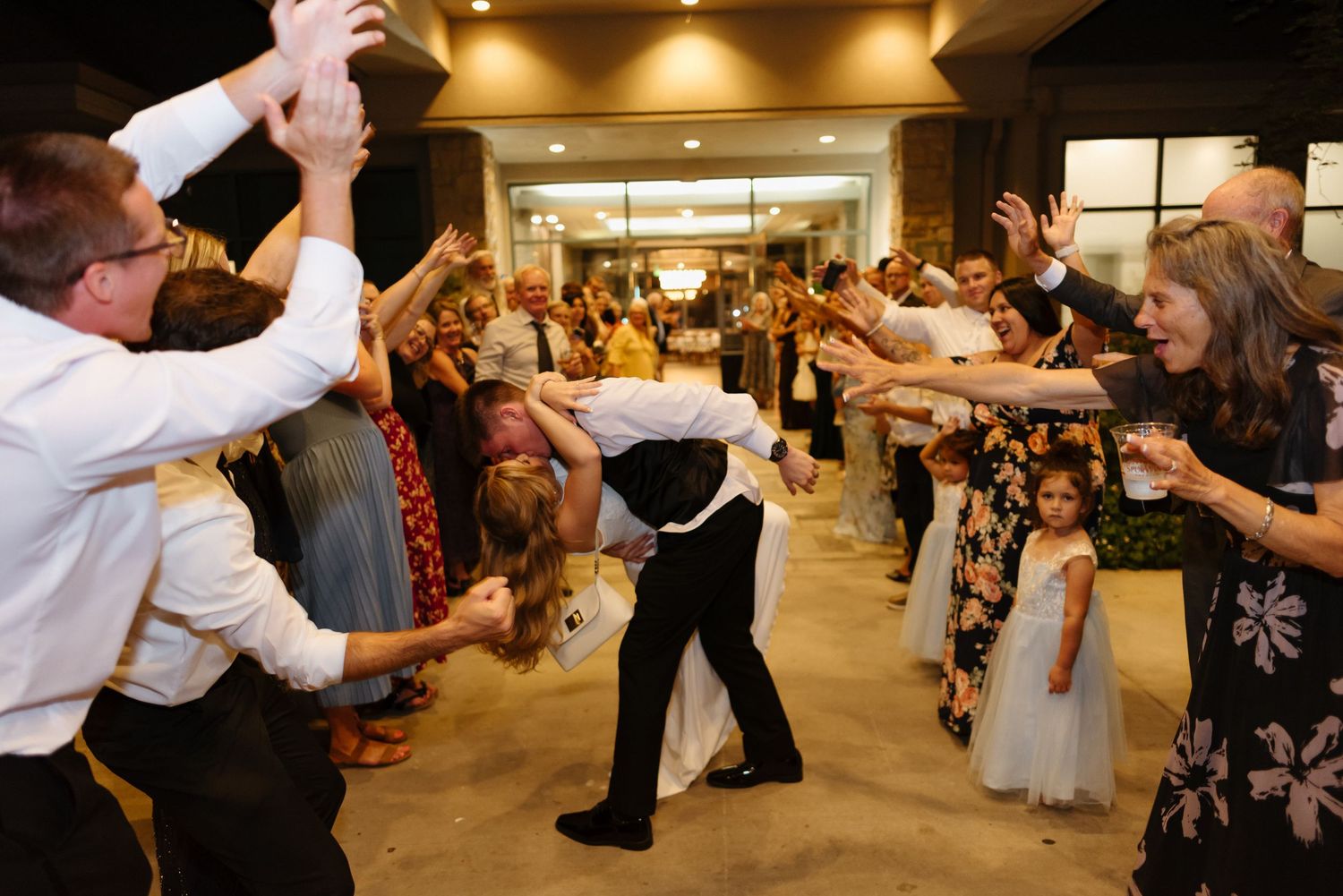 Wedding guests form a celebratory tunnel as bride and groom dance through at lively indoor reception.