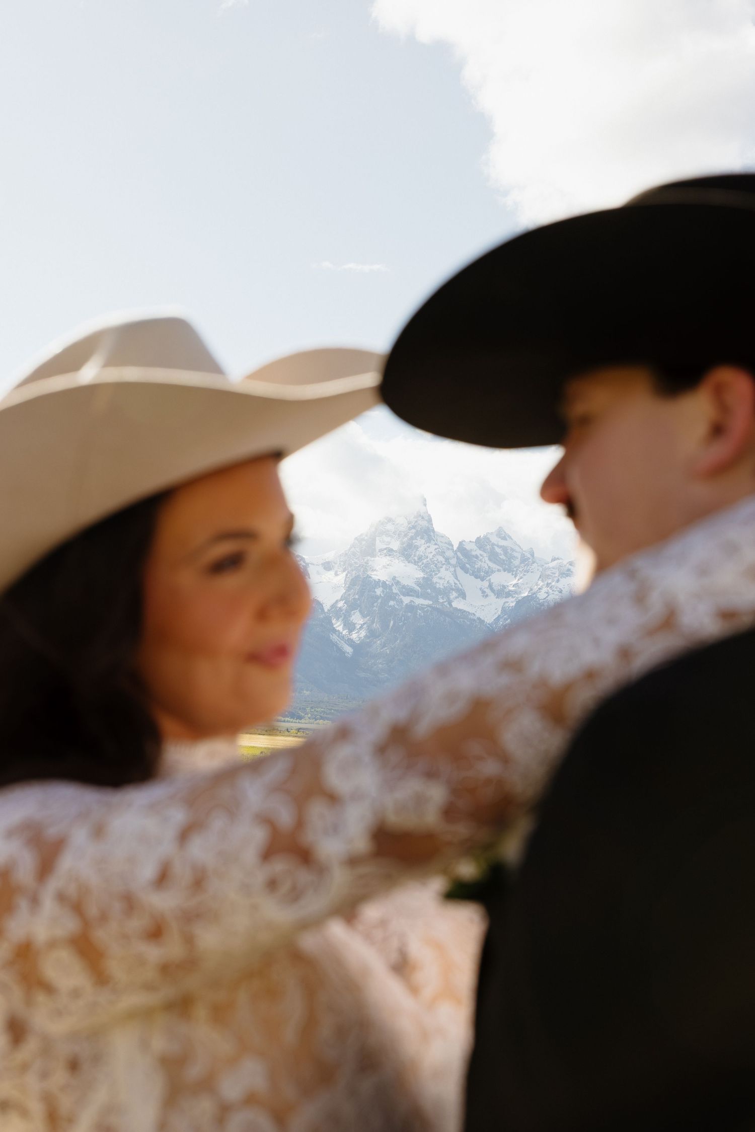 Bride and groom in cowboy hats share a romantic moment with the Grand Teton mountains in the background.