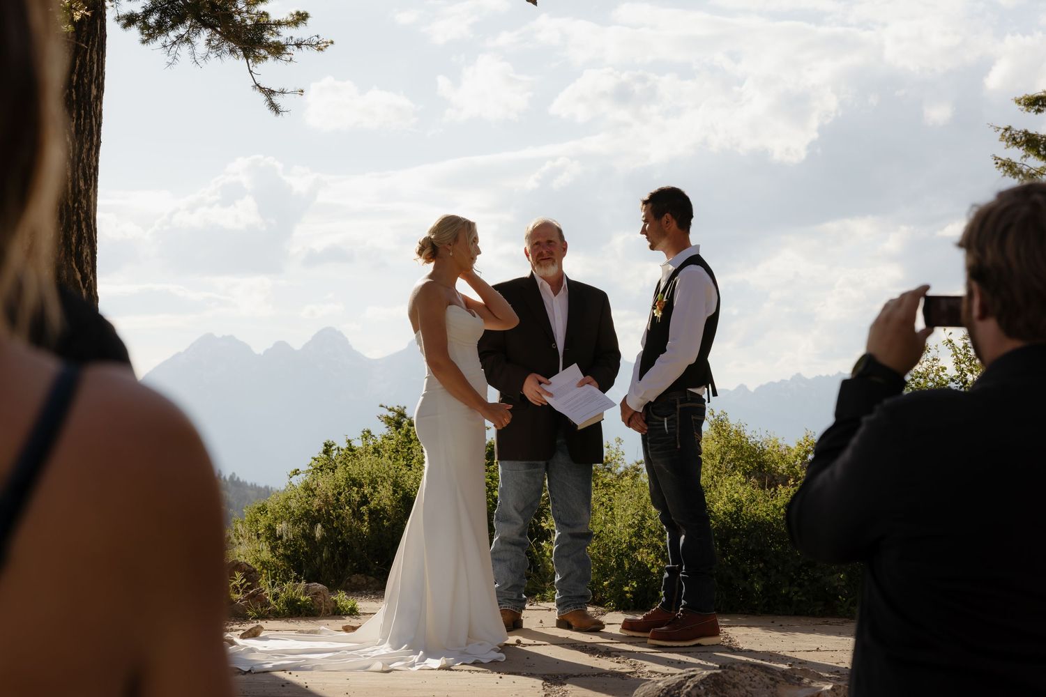Outdoor wedding ceremony with bride and groom exchanging vows before an officiant with mountain views.