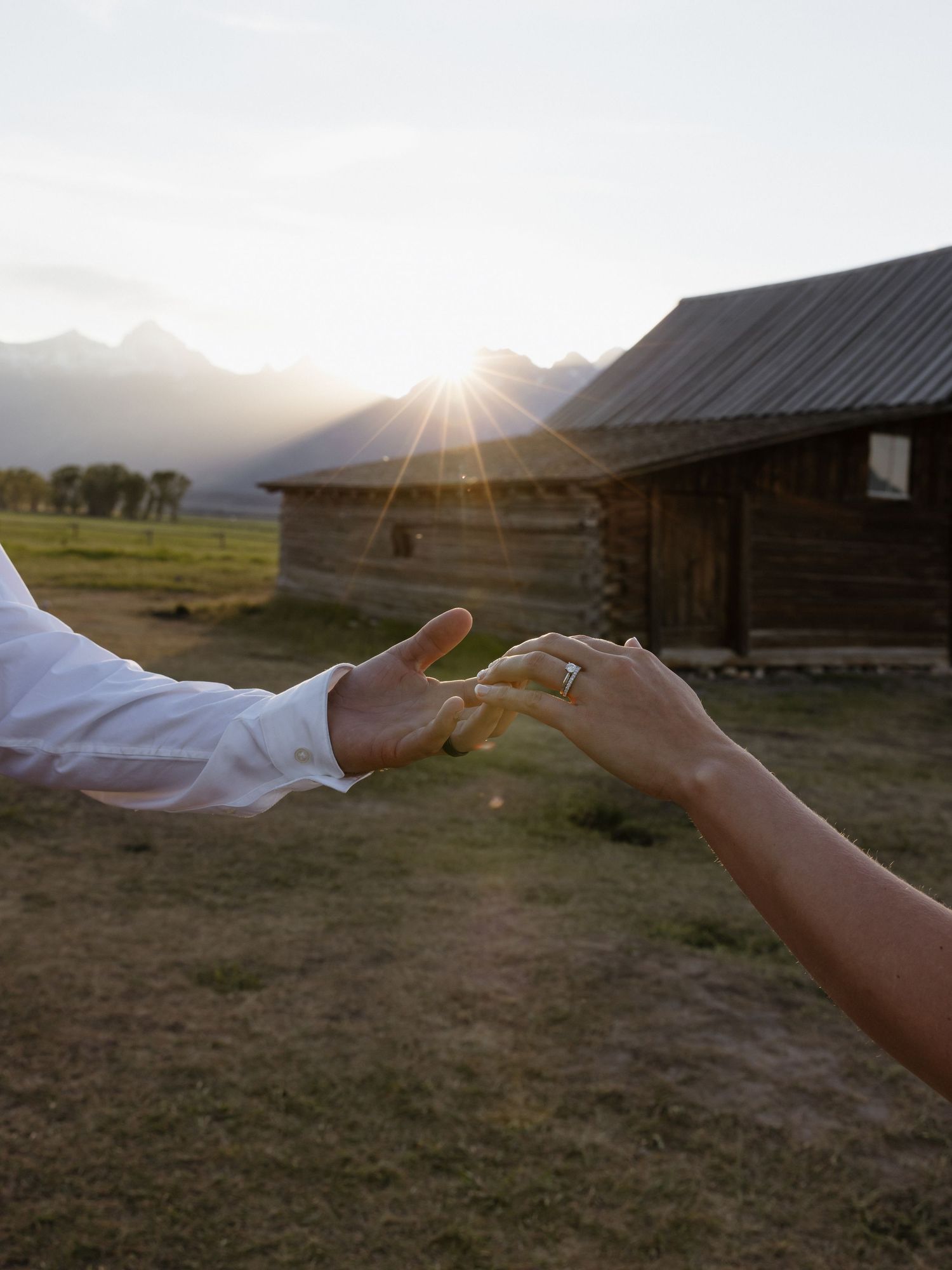 Close-up of bride and groom reaching hands toward each other with wedding ring visible at sunset.