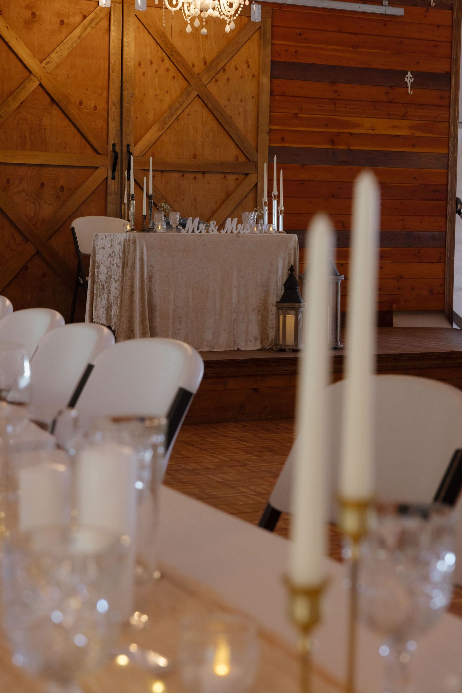 Elegant barn wedding reception with Mr. and Mrs. sweetheart table, white chairs, crystal glassware, and tall candles.