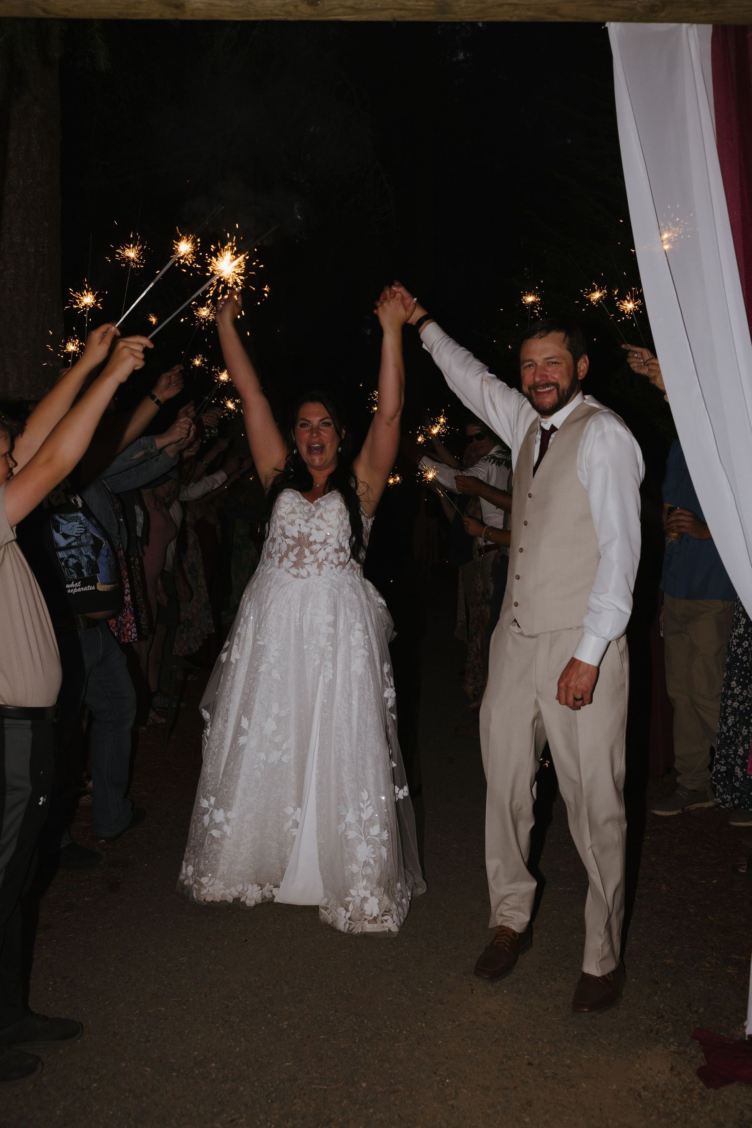 Bride and groom exit wedding reception through sparkler tunnel at night.