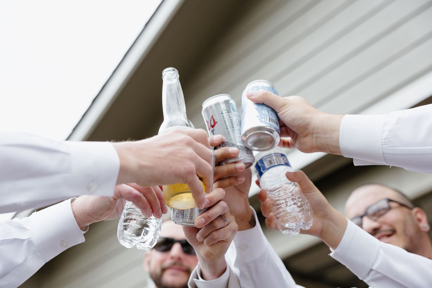 Groomsmen toasting with bottles and cans in a celebratory pre-wedding cheers from below angle.