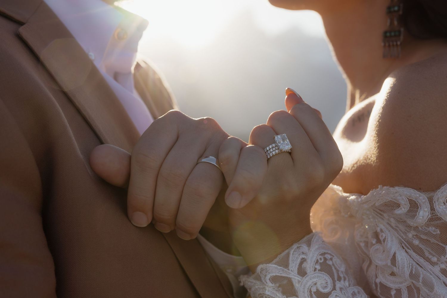 Close-up of newlyweds hands showing wedding rings in warm golden sunlight.