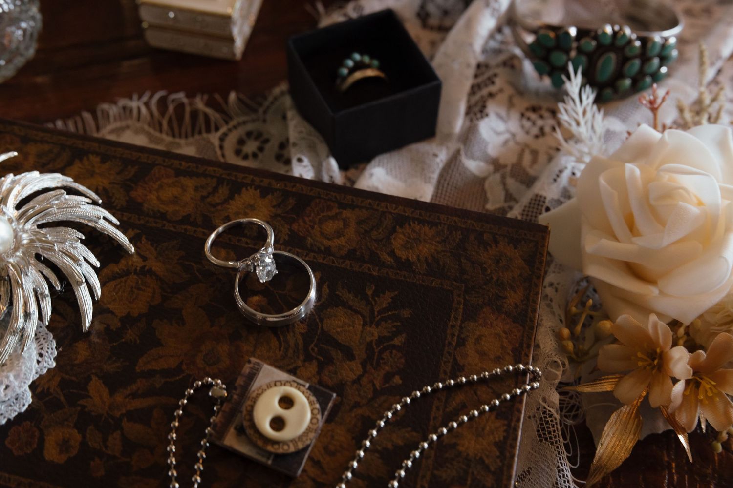 Vintage jewelry display with wedding rings, pearl necklace, and floral decorations on ornate wooden box.