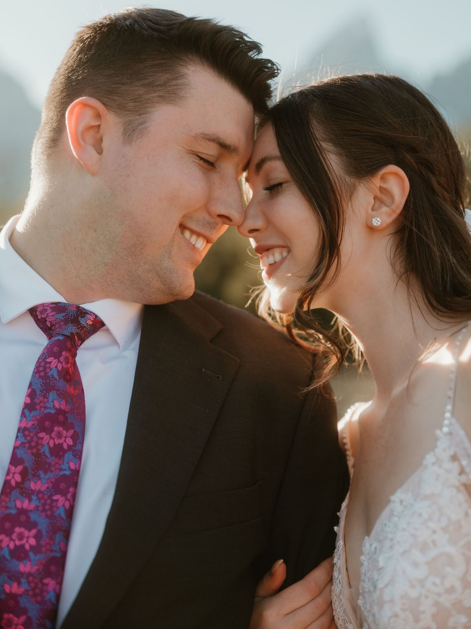 Happy bride and groom touch foreheads and smile in warm golden sunlight at their wedding celebration.