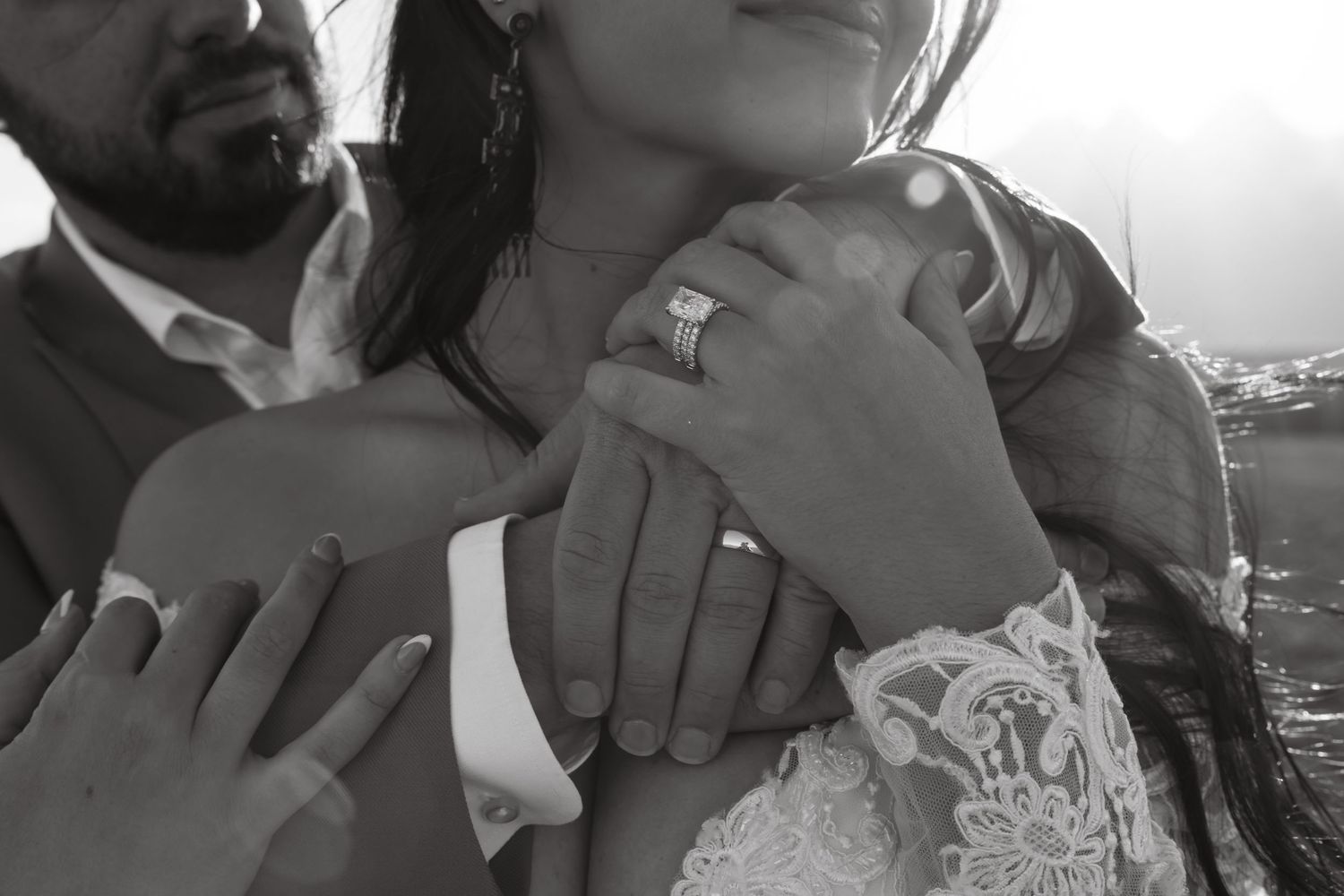 Black and white close-up of bride and groom hands showing wedding rings in tender embrace.