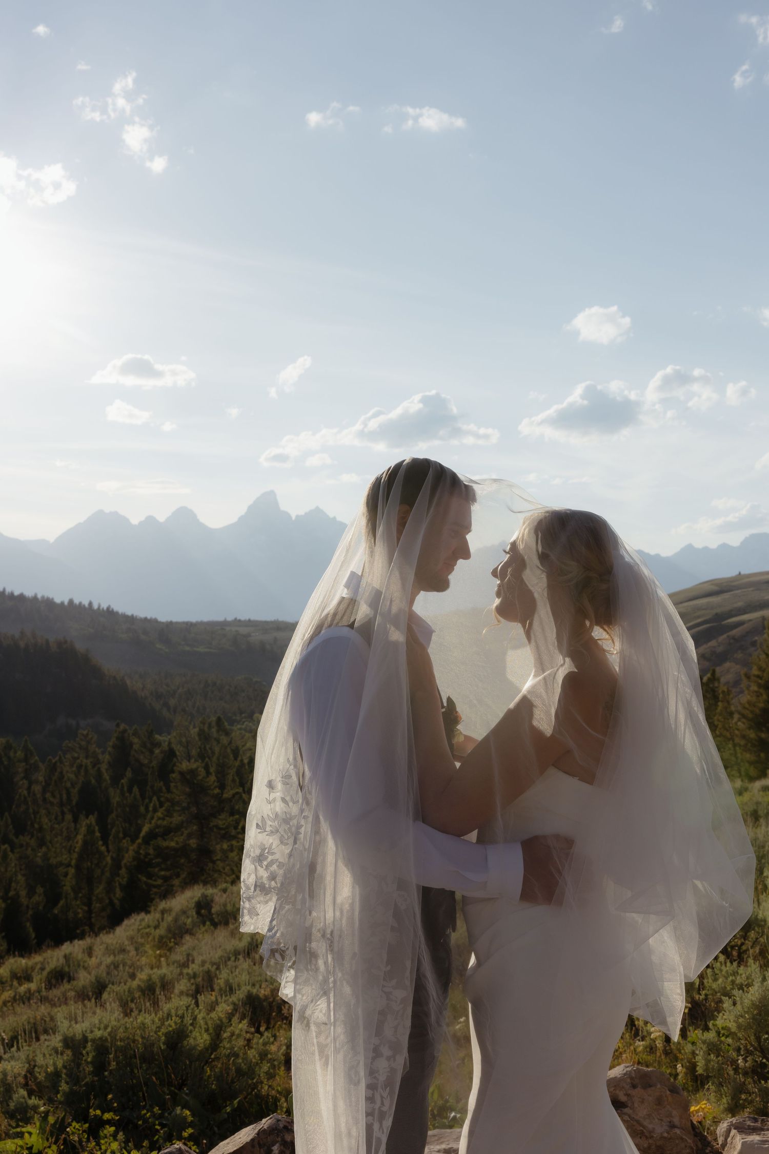 Bride and groom share an intimate moment under a flowing veil with Grand Teton mountains in the background.
