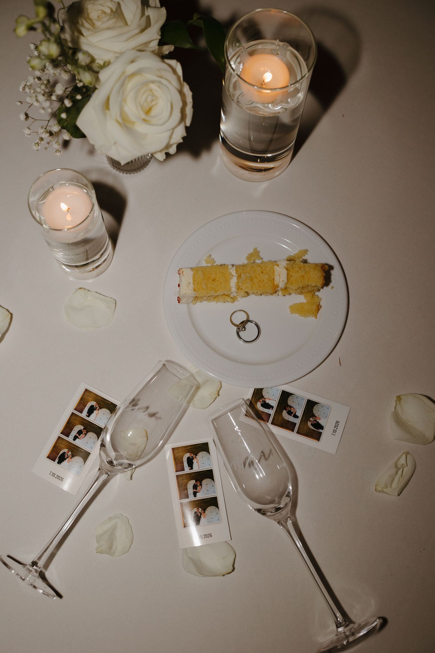 Overhead view of wedding reception table with champagne flutes, candles, wedding rings, cake, and photo booth strips.