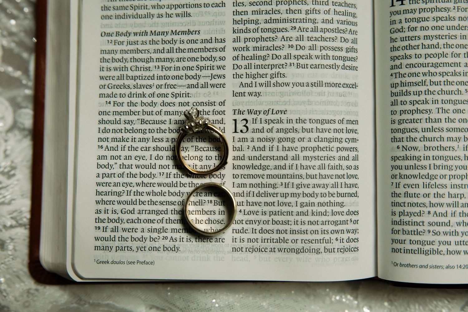Two gold wedding bands resting on an open Bible displaying 1 Corinthians 13.