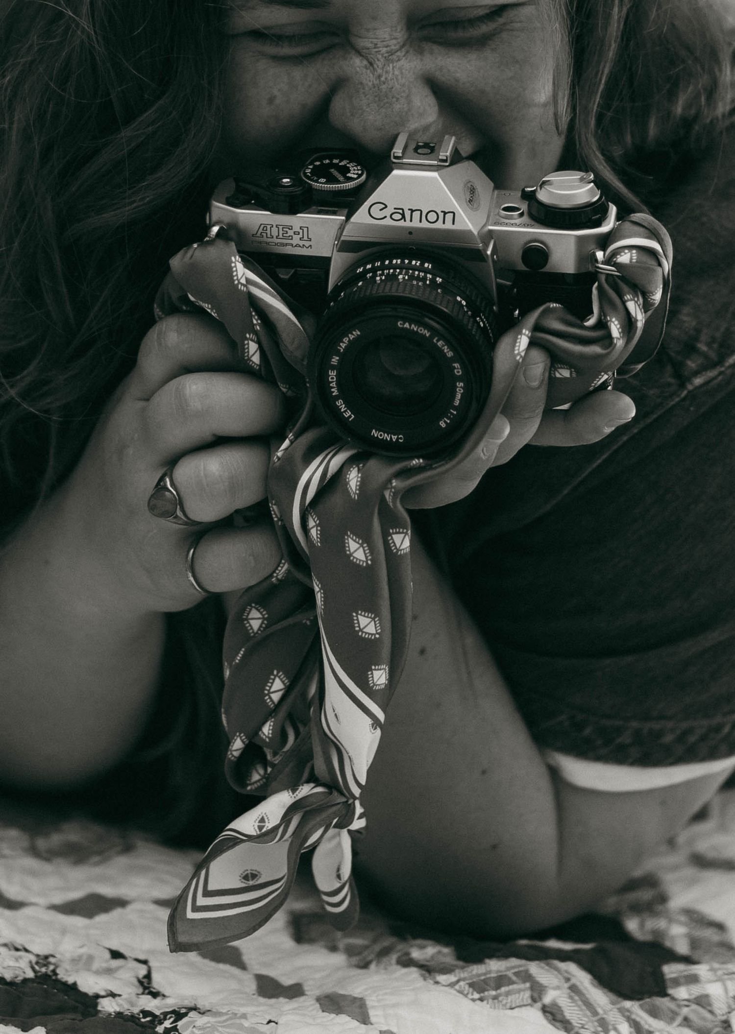 Black and white photo of smiling woman holding Canon AE-1 film camera close-up.