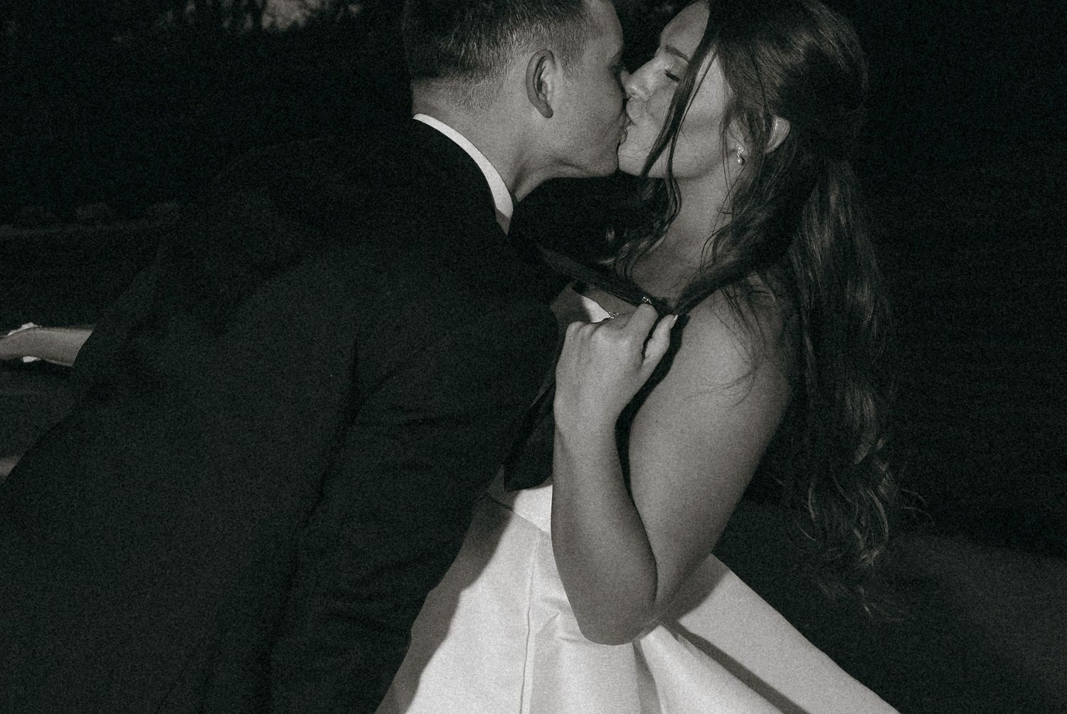 Black and white photo of bride and groom sharing a kiss at their wedding reception.