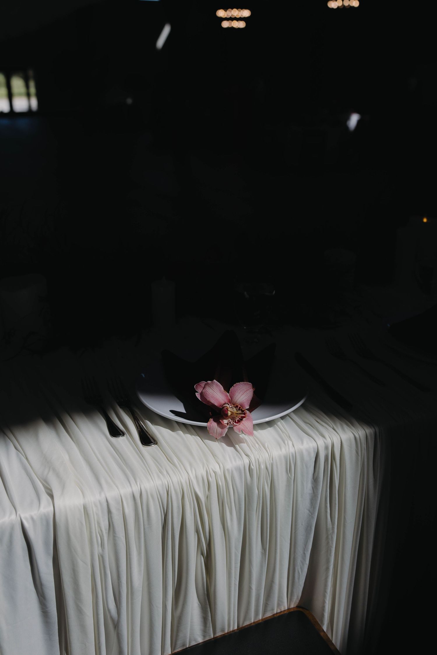 Single pink flower on white plate at elegantly draped dark wedding reception table.