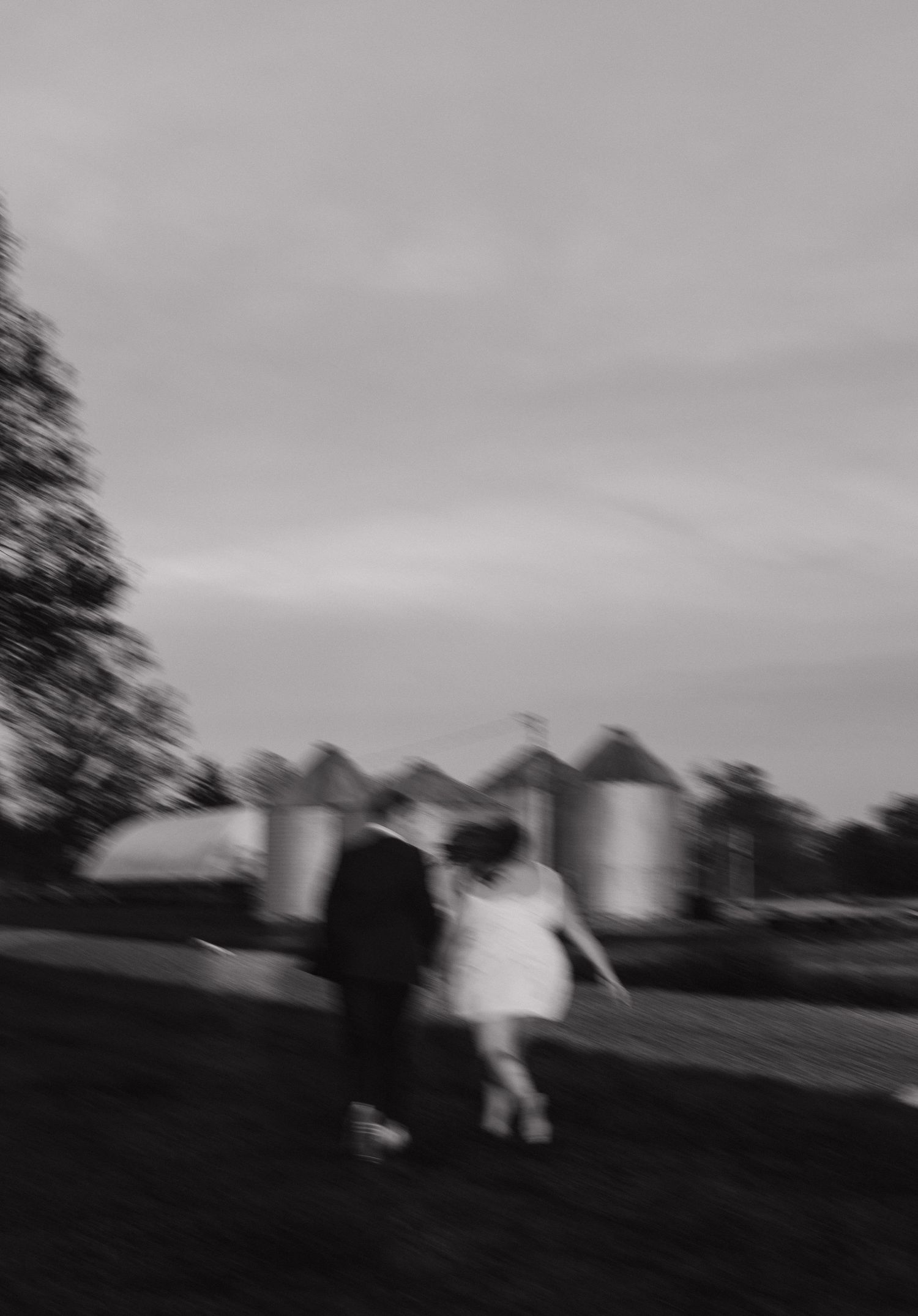Black and white blurred motion photo of couple walking near rustic farm silos.