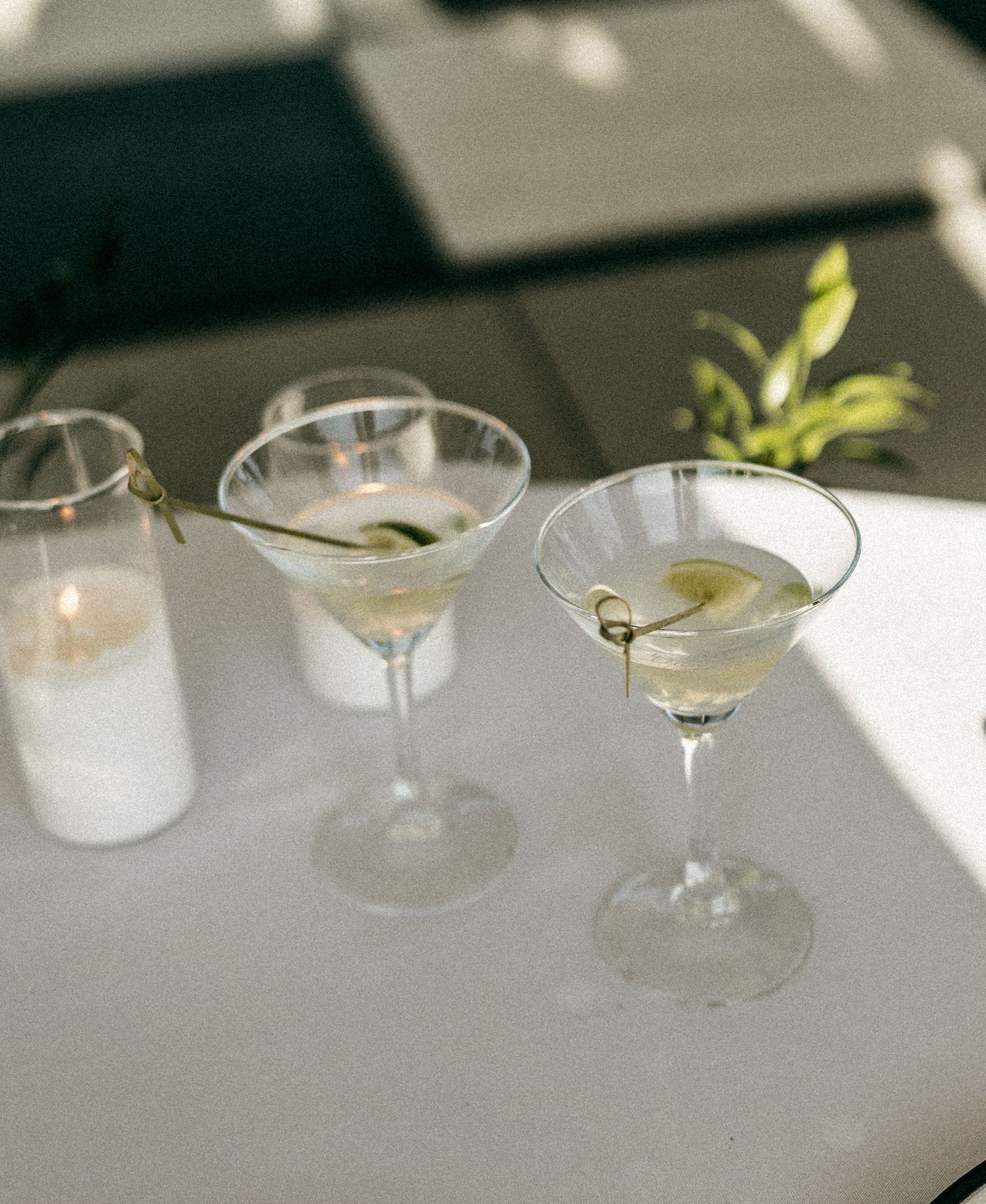 Two elegant martini cocktails with cucumber garnish on a sunlit white table.