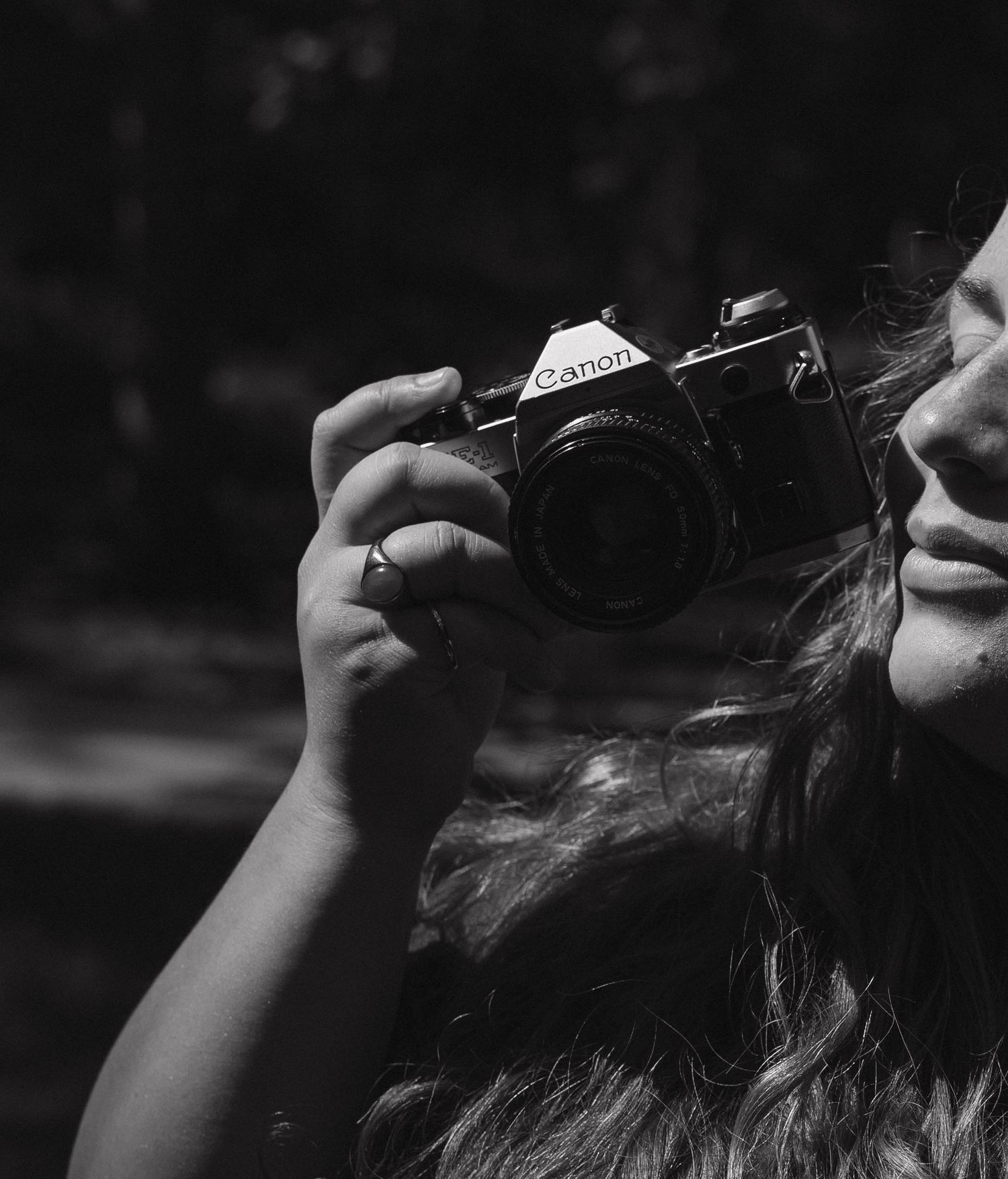 Black and white portrait of a woman holding a Canon film camera to her face.
