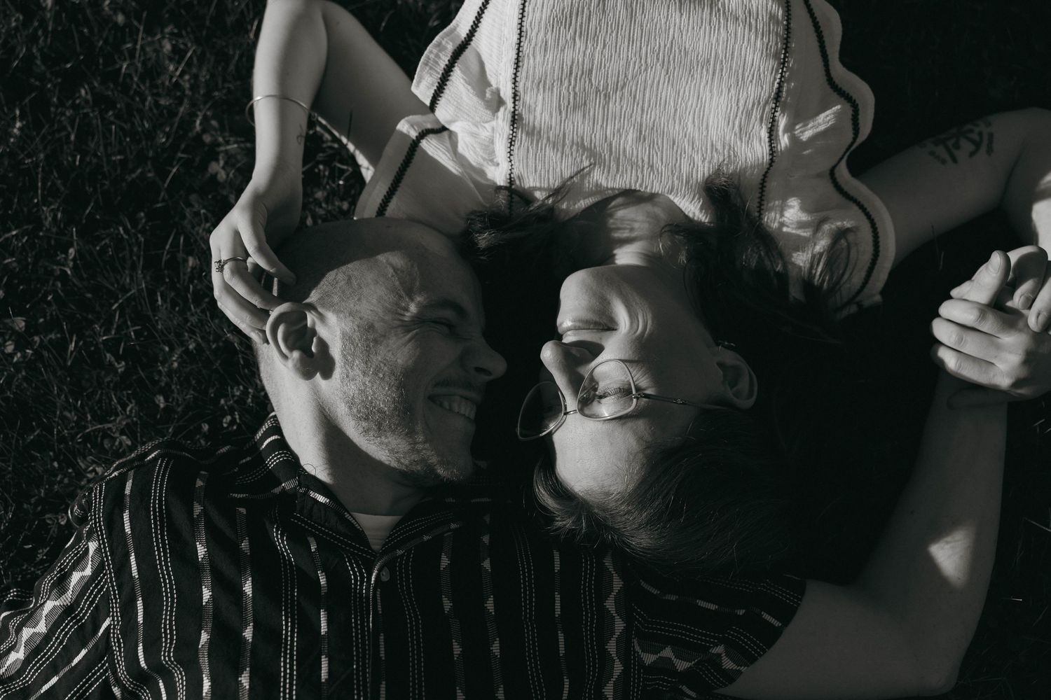 Black and white overhead view of smiling couple lying on grass looking at each other.