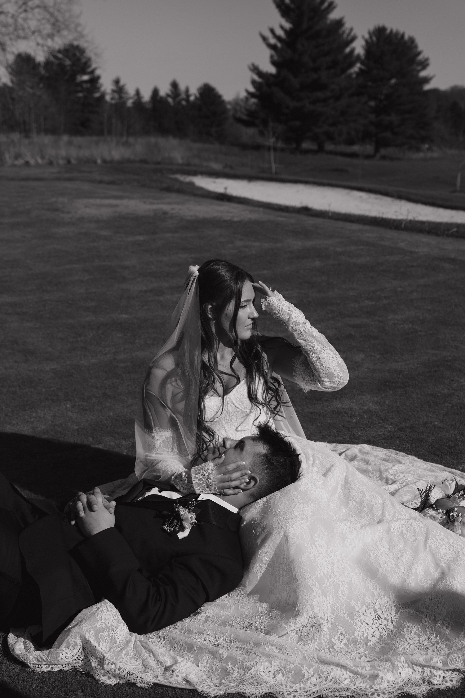 Black and white photo of bride and groom relaxing on grass at a golf course on their wedding day.