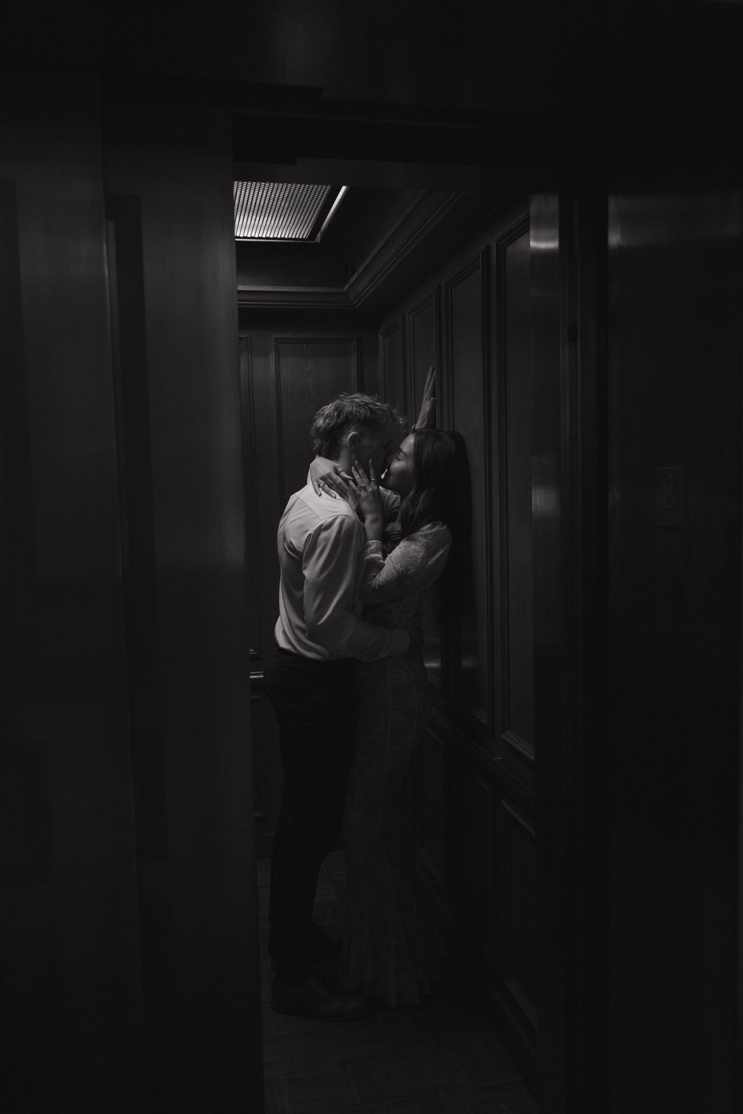 Black and white romantic couple embracing and kissing in a dimly lit hallway.