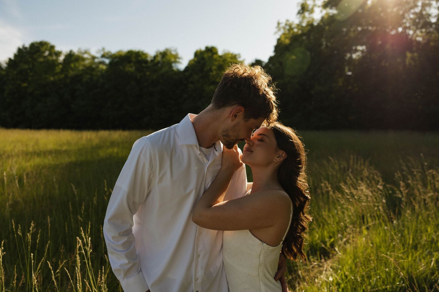 Couple sharing a tender almost-kiss in a golden sunlit green meadow.