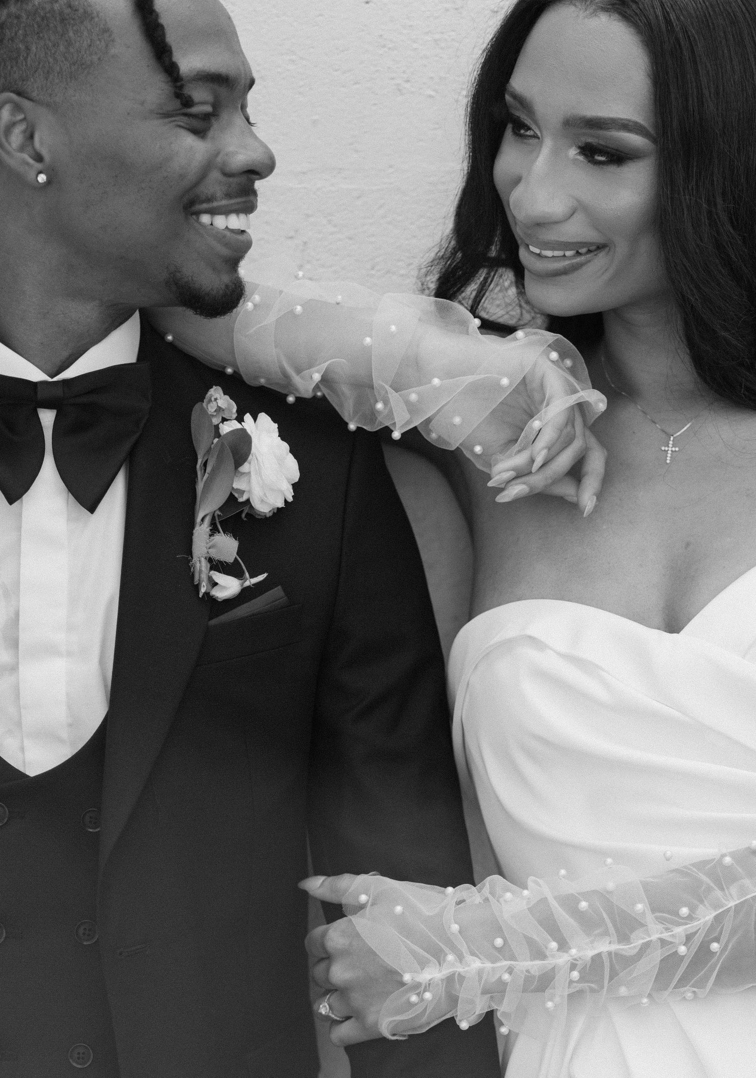 Black and white wedding photo of a smiling couple, groom in tuxedo and bride in strapless gown with sheer gloves.
