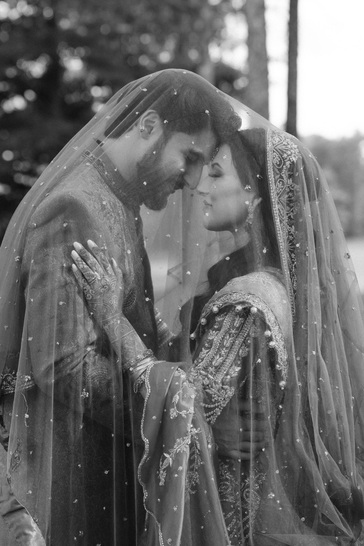 Black and white photo of South Asian bride and groom sharing an intimate moment under a pearl-adorned veil.
