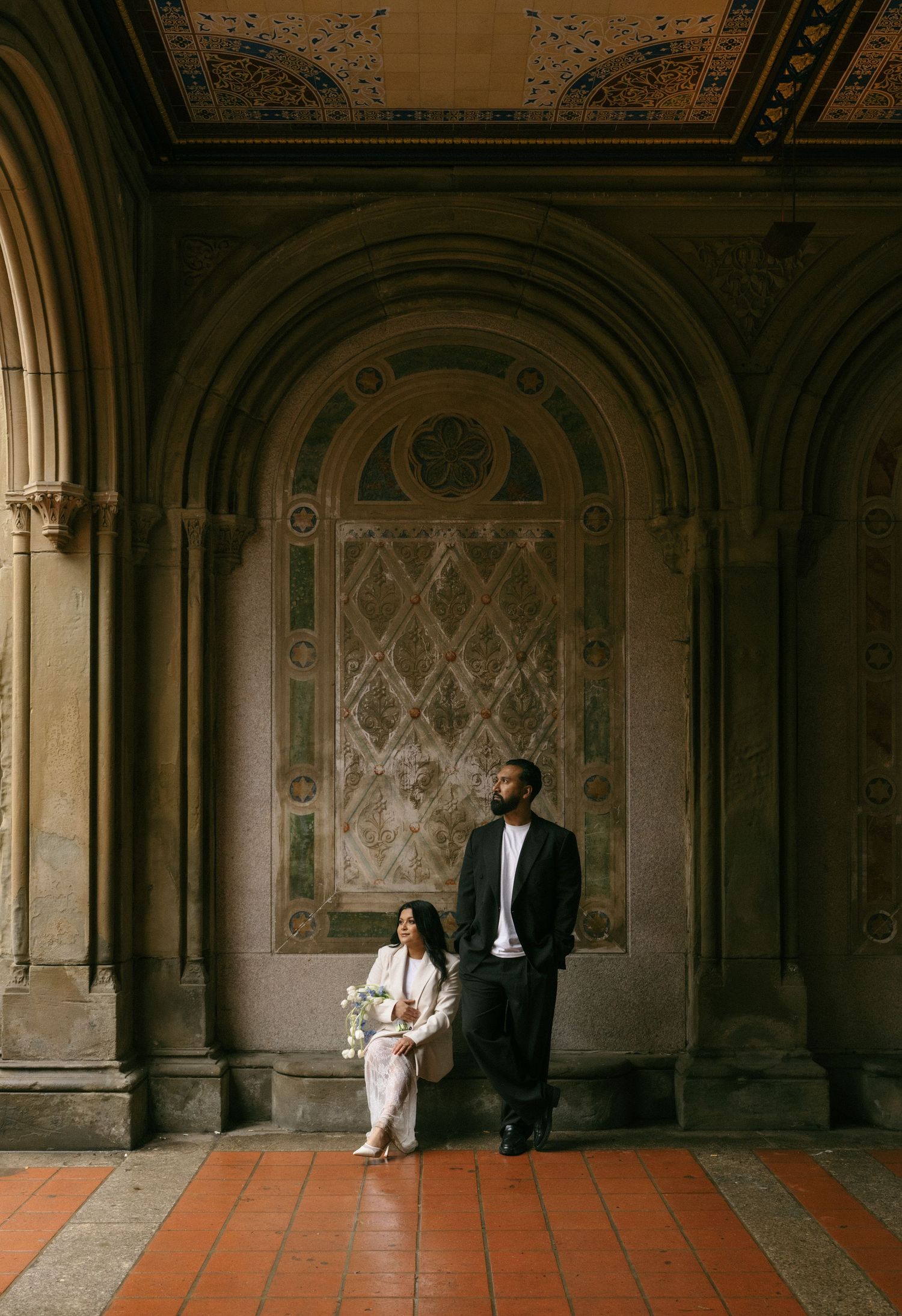 Bride and groom posing at ornate Bethesda Terrace archway in Central Park, New York.