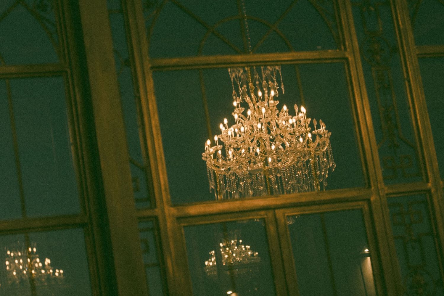 Elegant crystal chandelier hanging from an ornate gold ceiling in a grand ballroom with green walls.