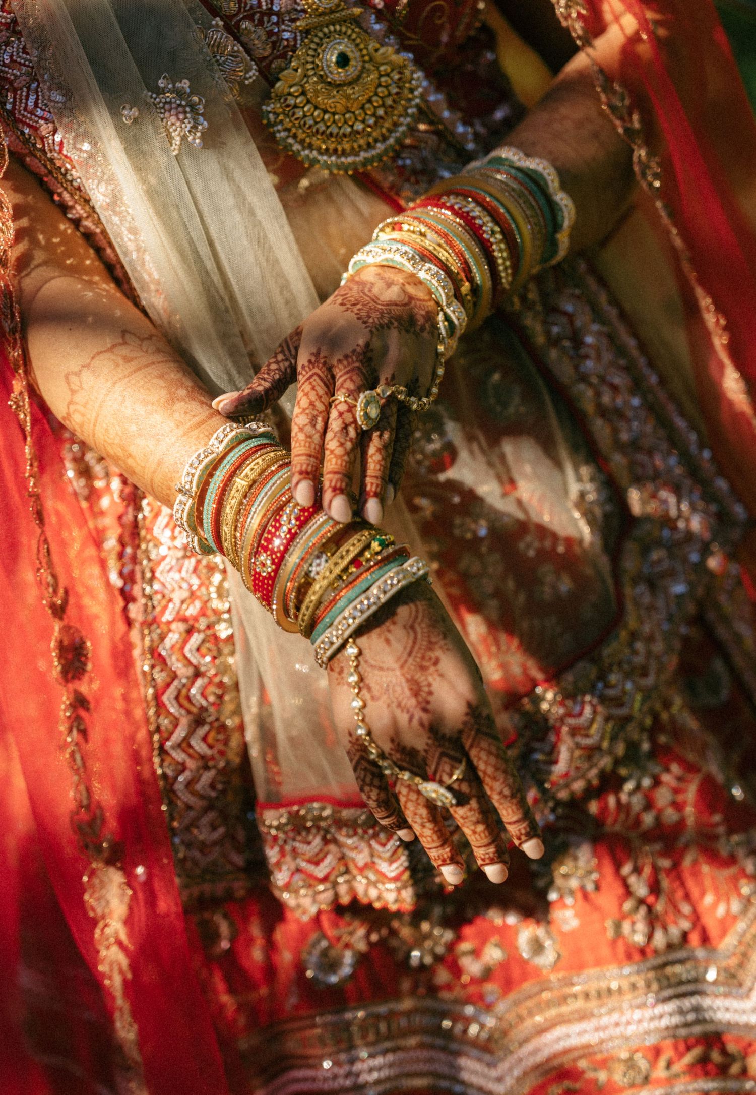 Bride displaying traditional Indian bridal henna mehndi hands with colorful bangles and red lehenga.